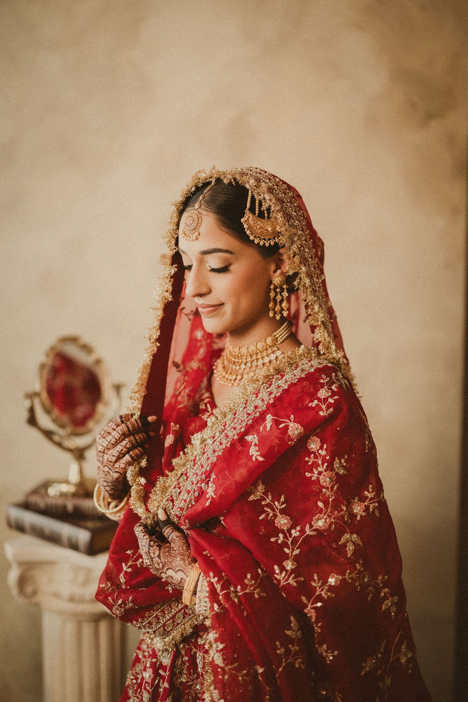 Traditional Indian bride wearing ornate red and gold embroidered lehenga and heavy bridal jewelry in vintage-style portraits.
