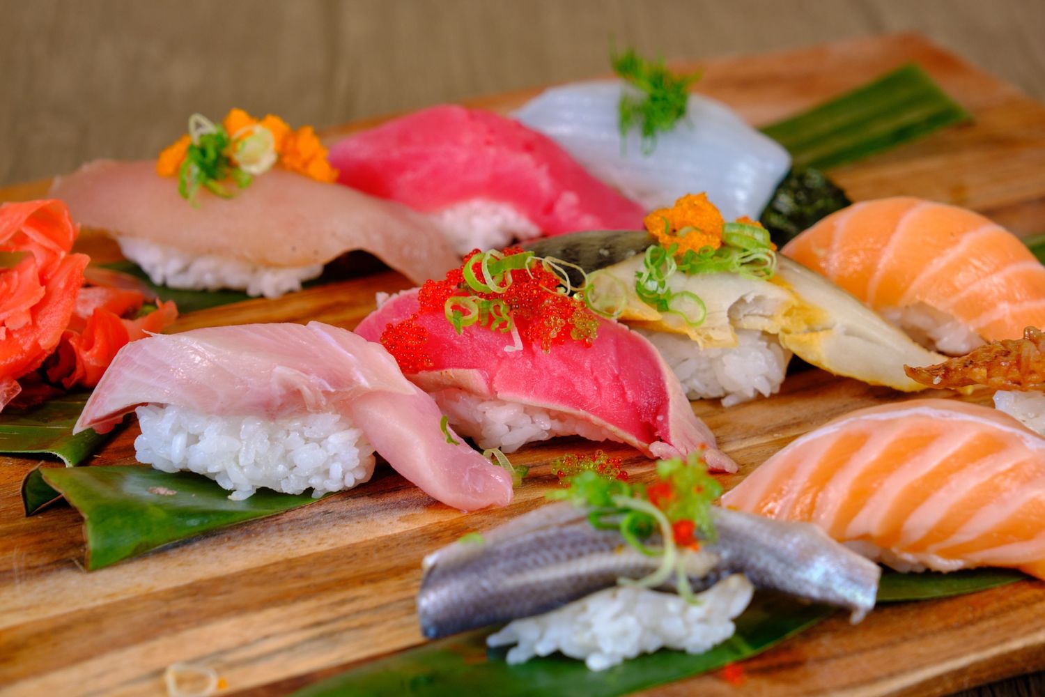 Colorful assortment of fresh sushi nigiri served on wooden board with garnishes.