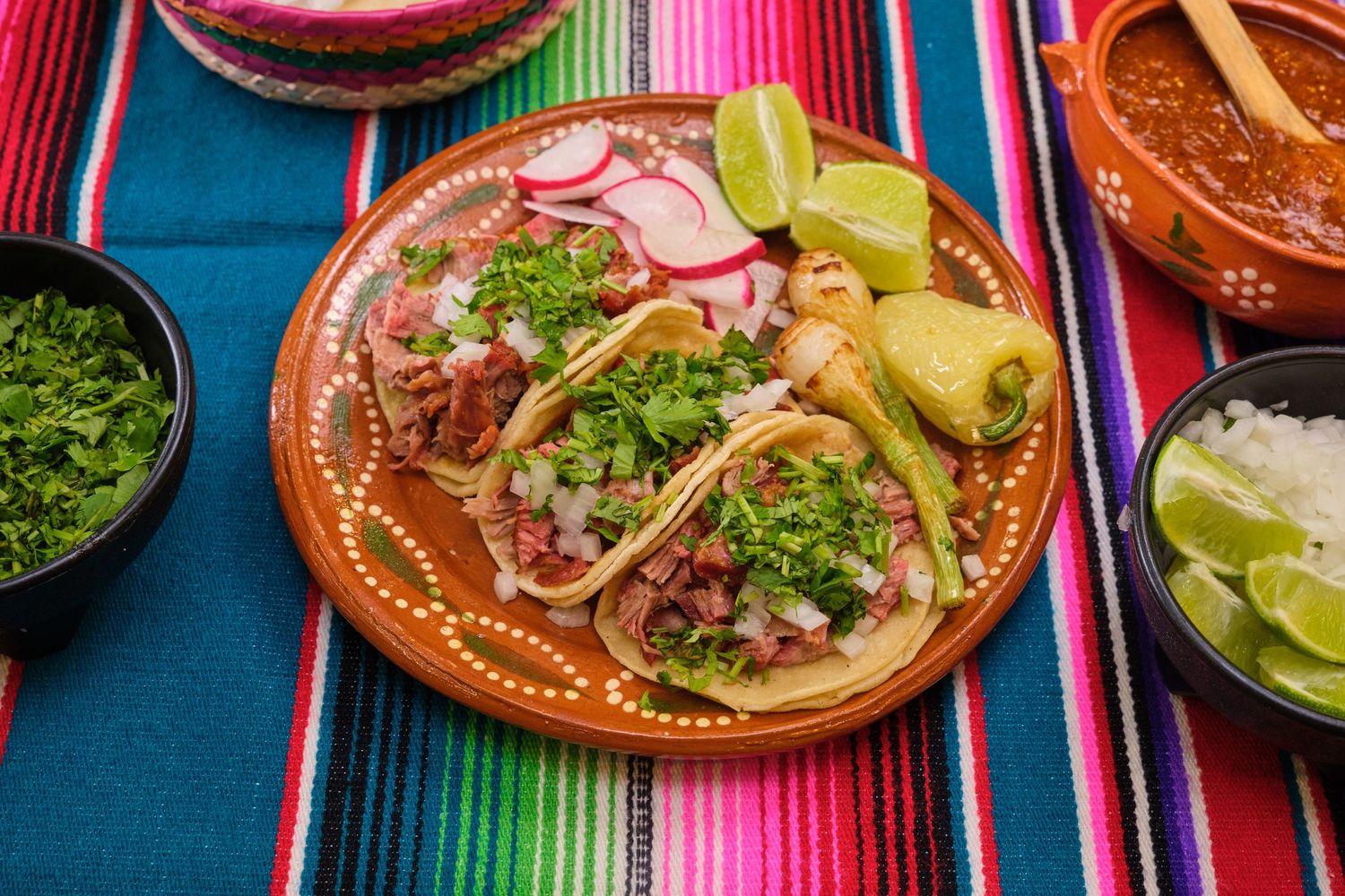 Street tacos garnished with cilantro and lime on a traditional Mexican clay plate.