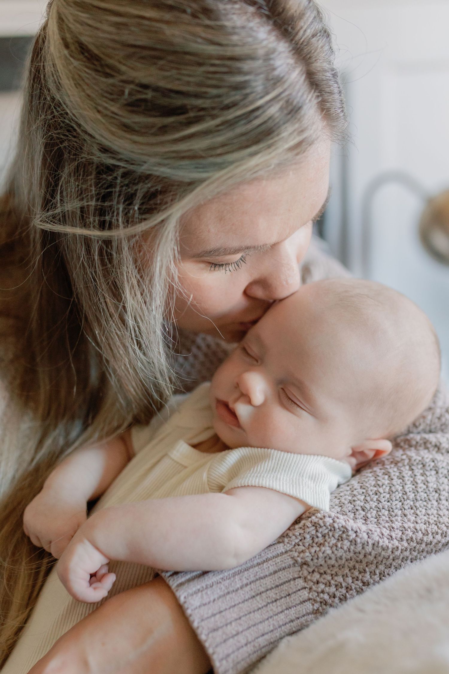 A woman holds her newborn, gently kissing him on his head. Moment captured by Katie Crane.