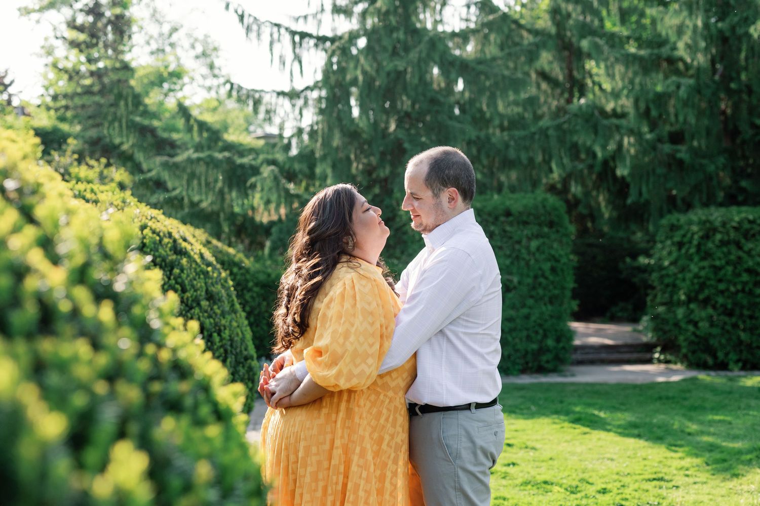 Couple sharing tender embrace in garden setting with golden sunlight.