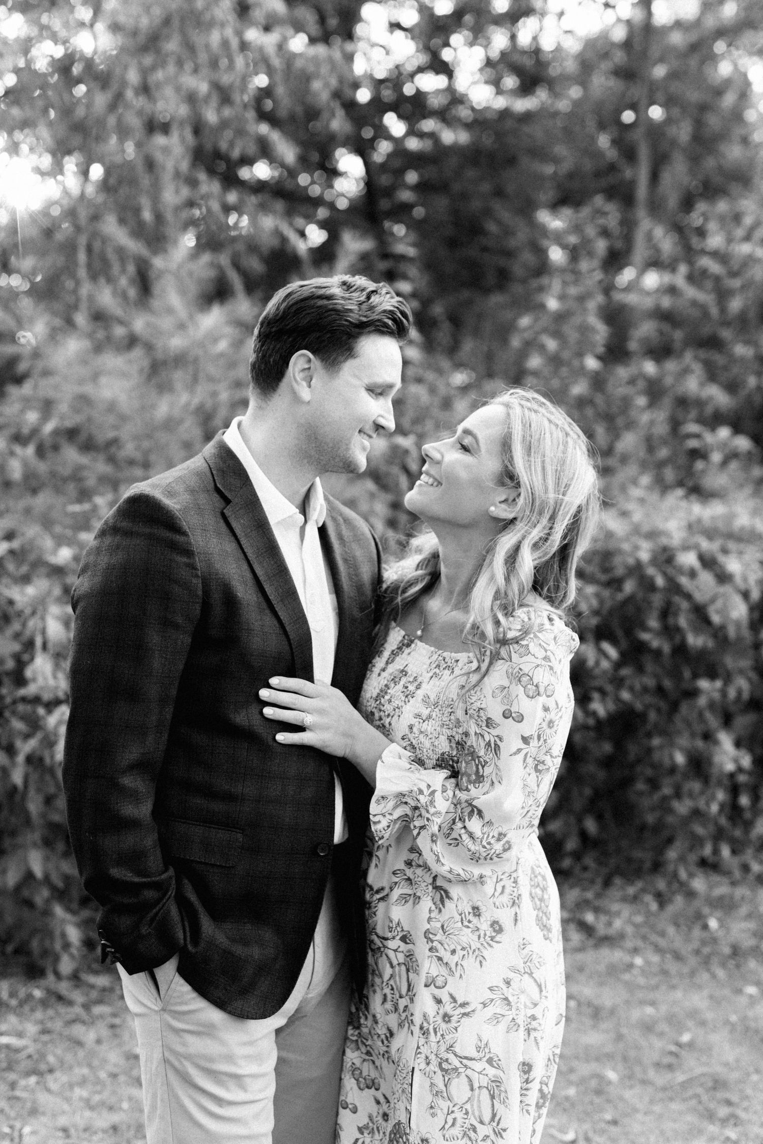 A couple in formal attire shares an intimate moment outdoors in black and white photography.