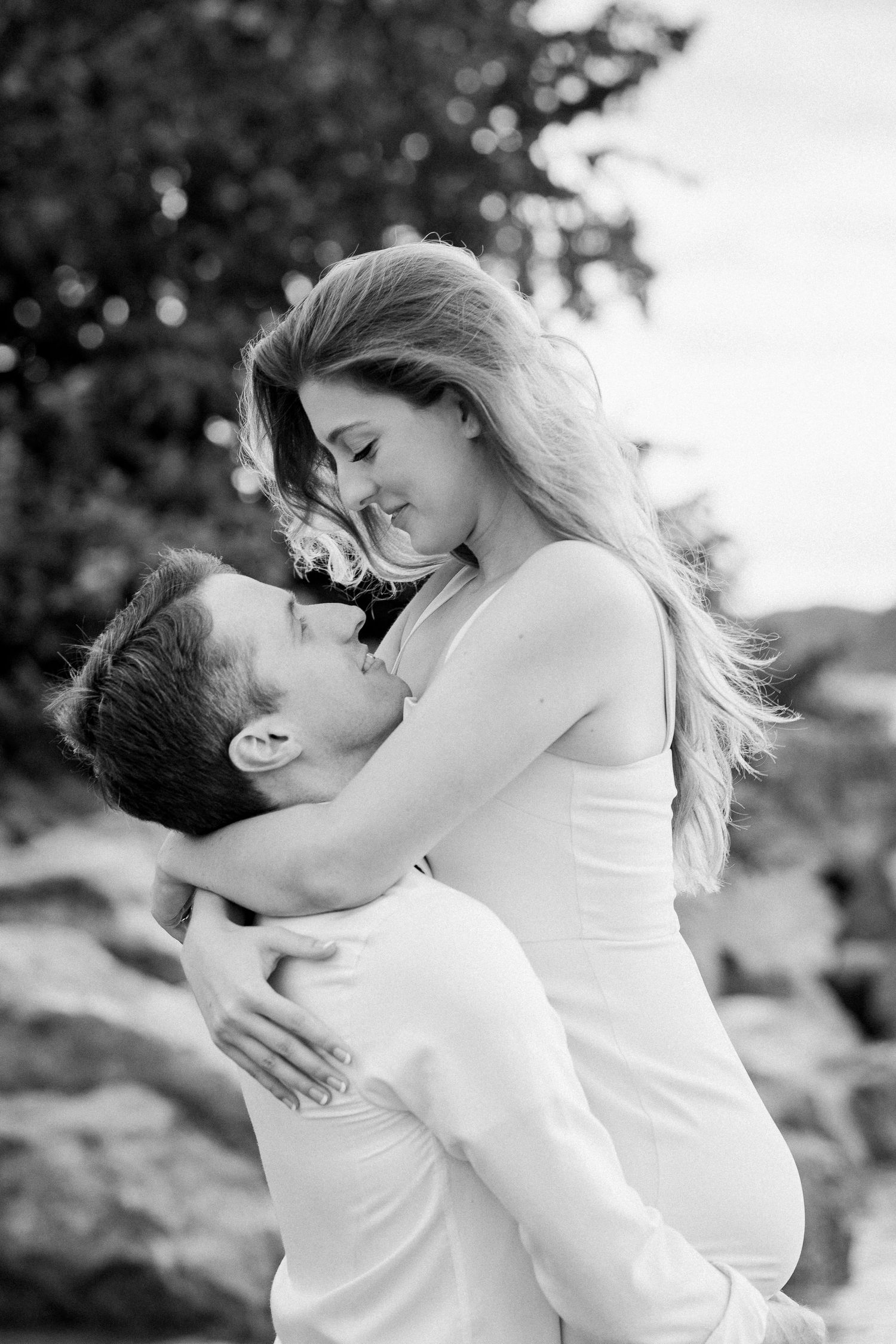 Intimate black and white portrait of couple embracing against natural backdrop.