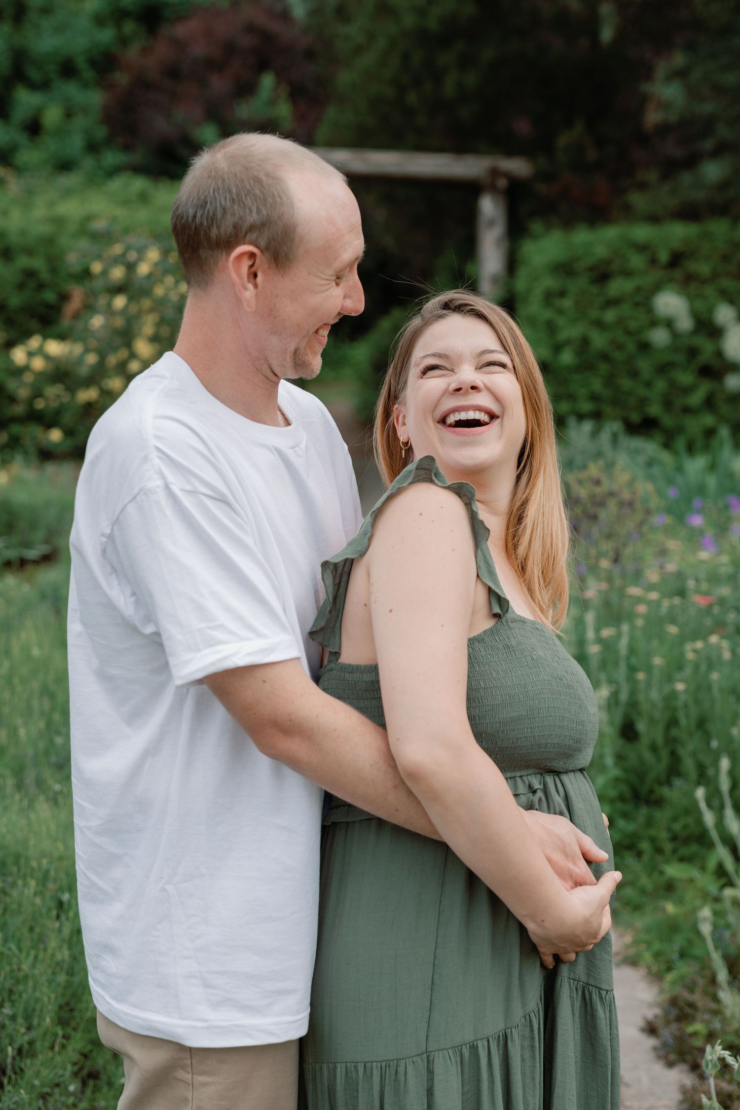 A couple shares candid moments of laughter in a blooming garden setting.