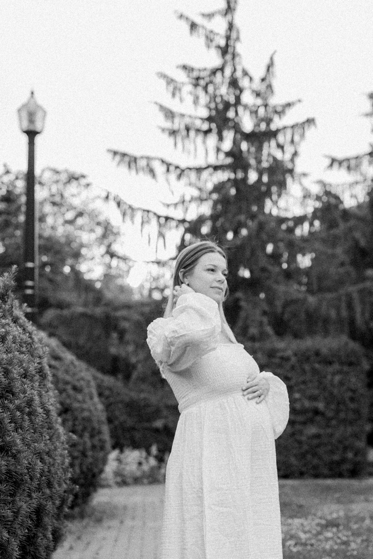 Black and white photo of a couple embracing in a romantic outdoor setting with evergreen trees.