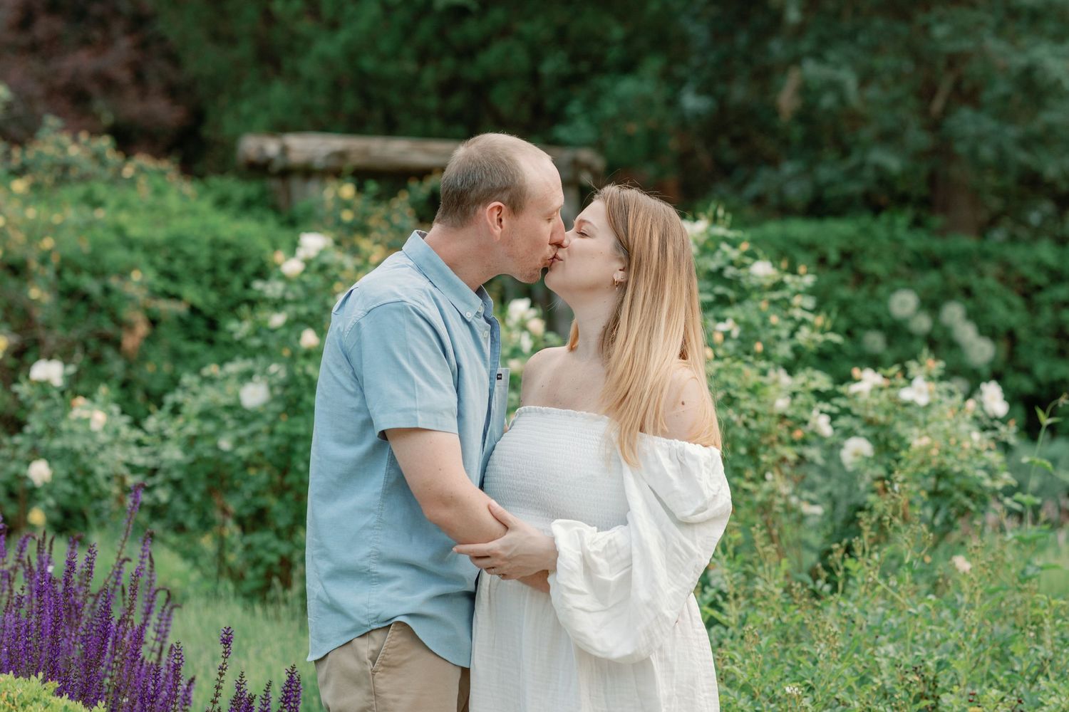 A couple embraces tenderly in a summer garden filled with colorful wildflowers and greenery.