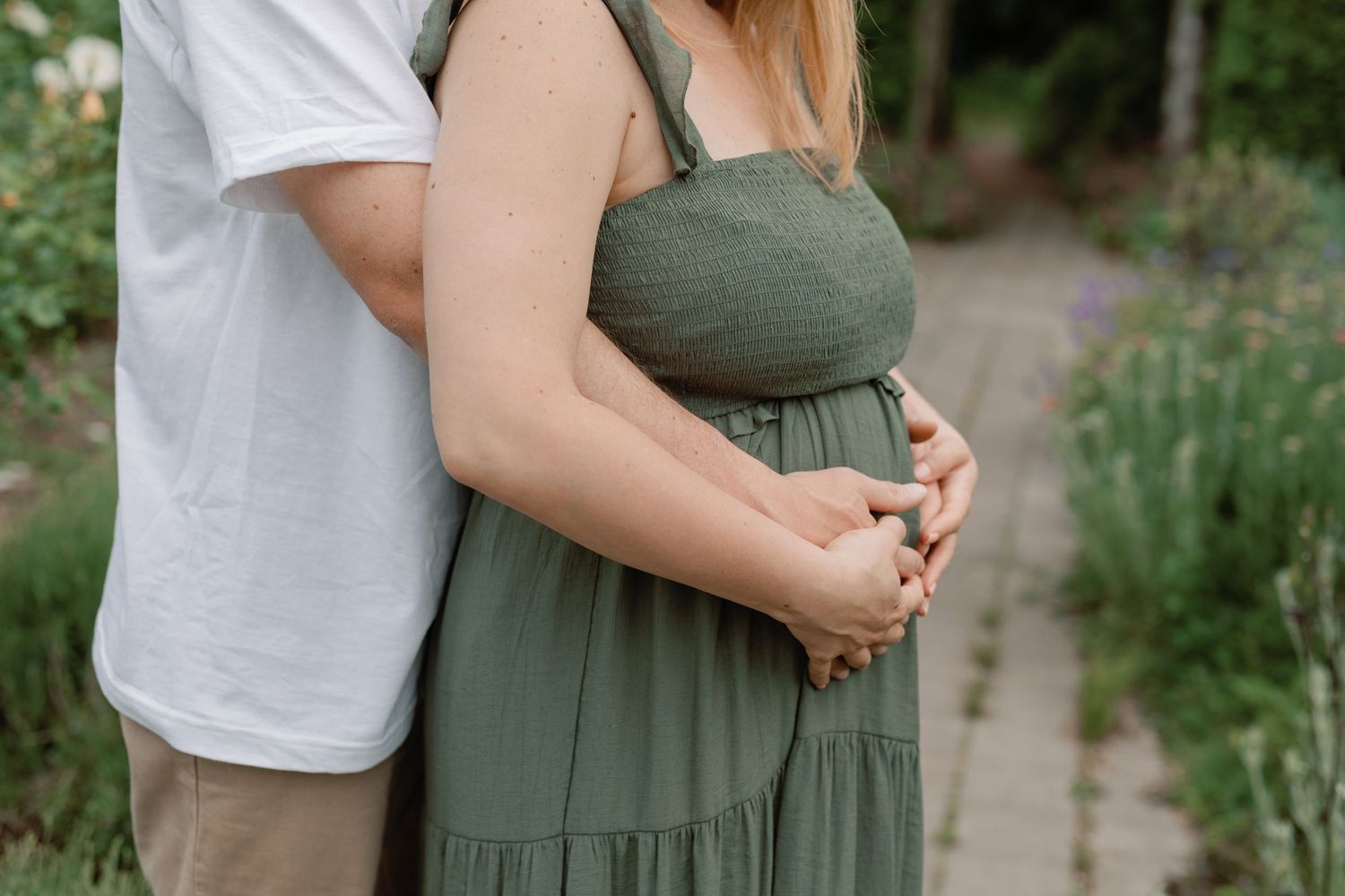 Couple in casual attire shares tender moment in blooming garden setting.