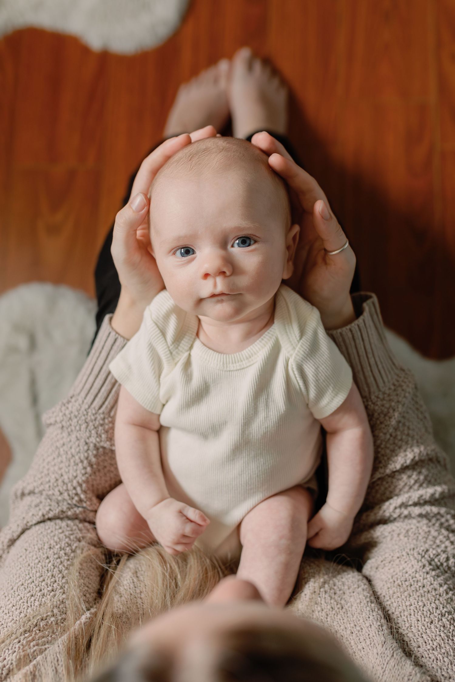 Baby looking up at the camera, his head is cradled in his mother's hands. Photo: Katie Crane Photography.
