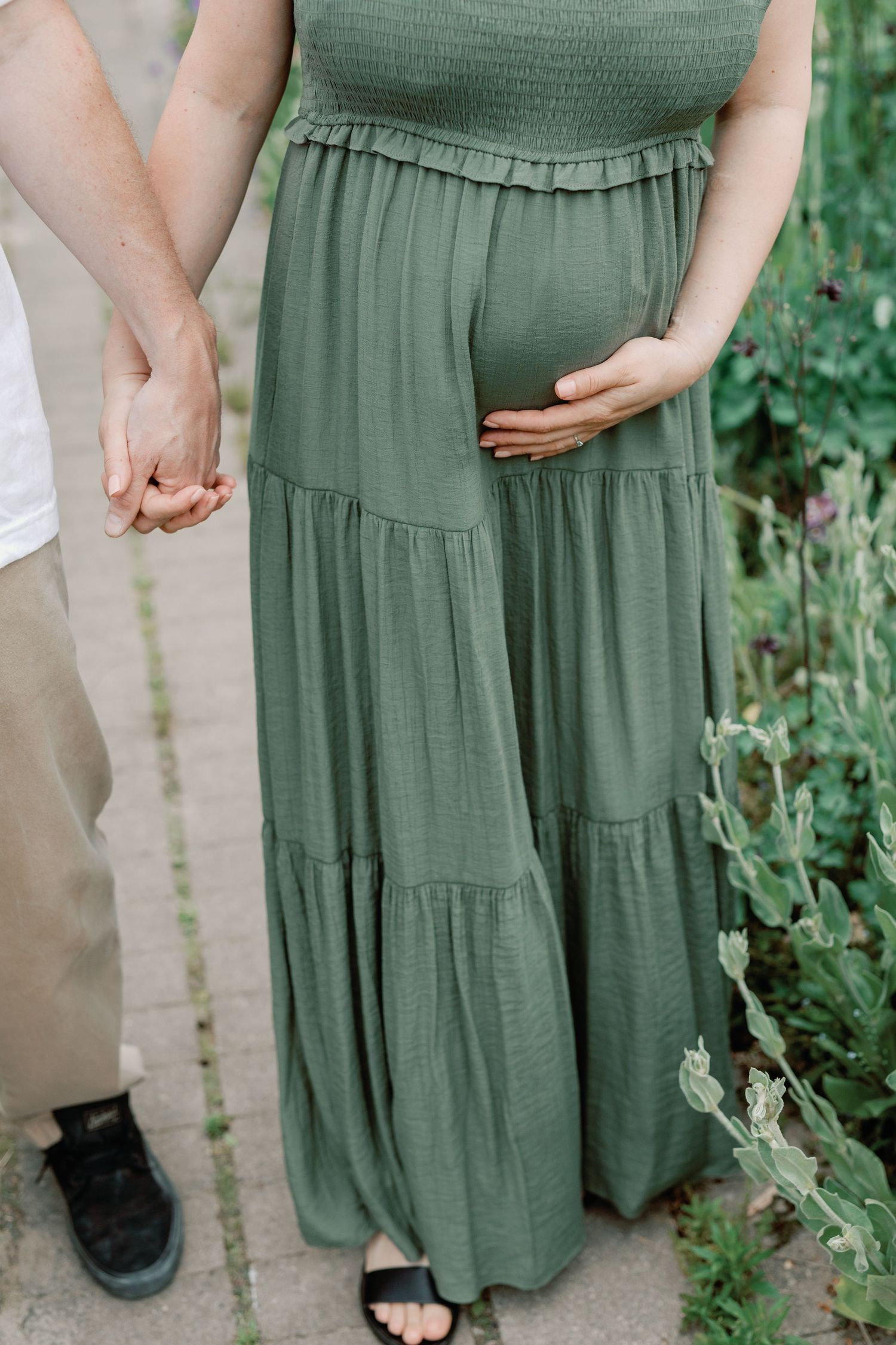 Close-up shots of couple holding hands in garden wearing green dress.