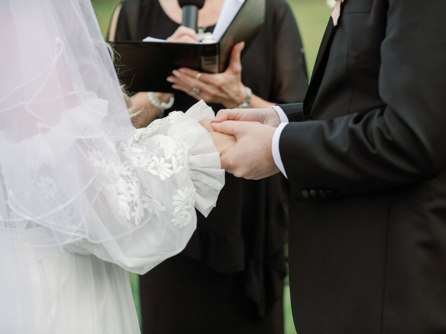 A close up shot of a bride and groom holding hands at the alter, the officiant behind them reading vows at Cave Springs 