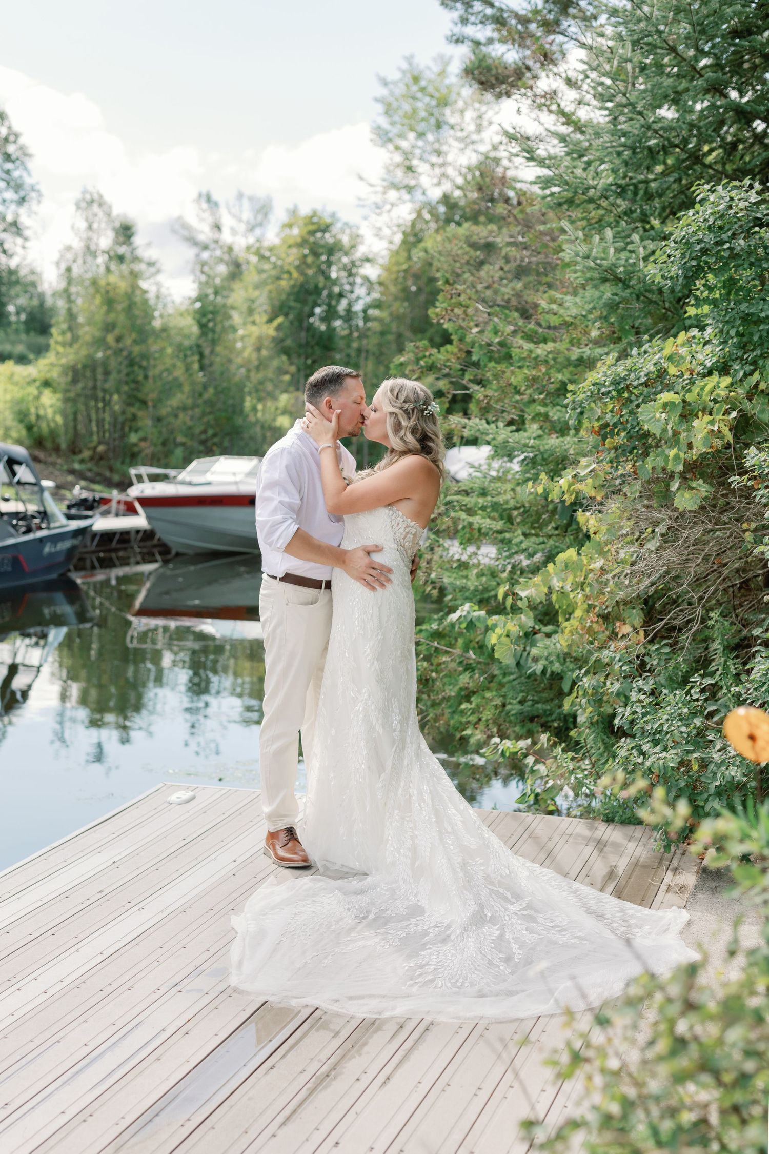 A couple in wedding attire share a kiss standing on their dock. Photo taken by Katie Crane Photography