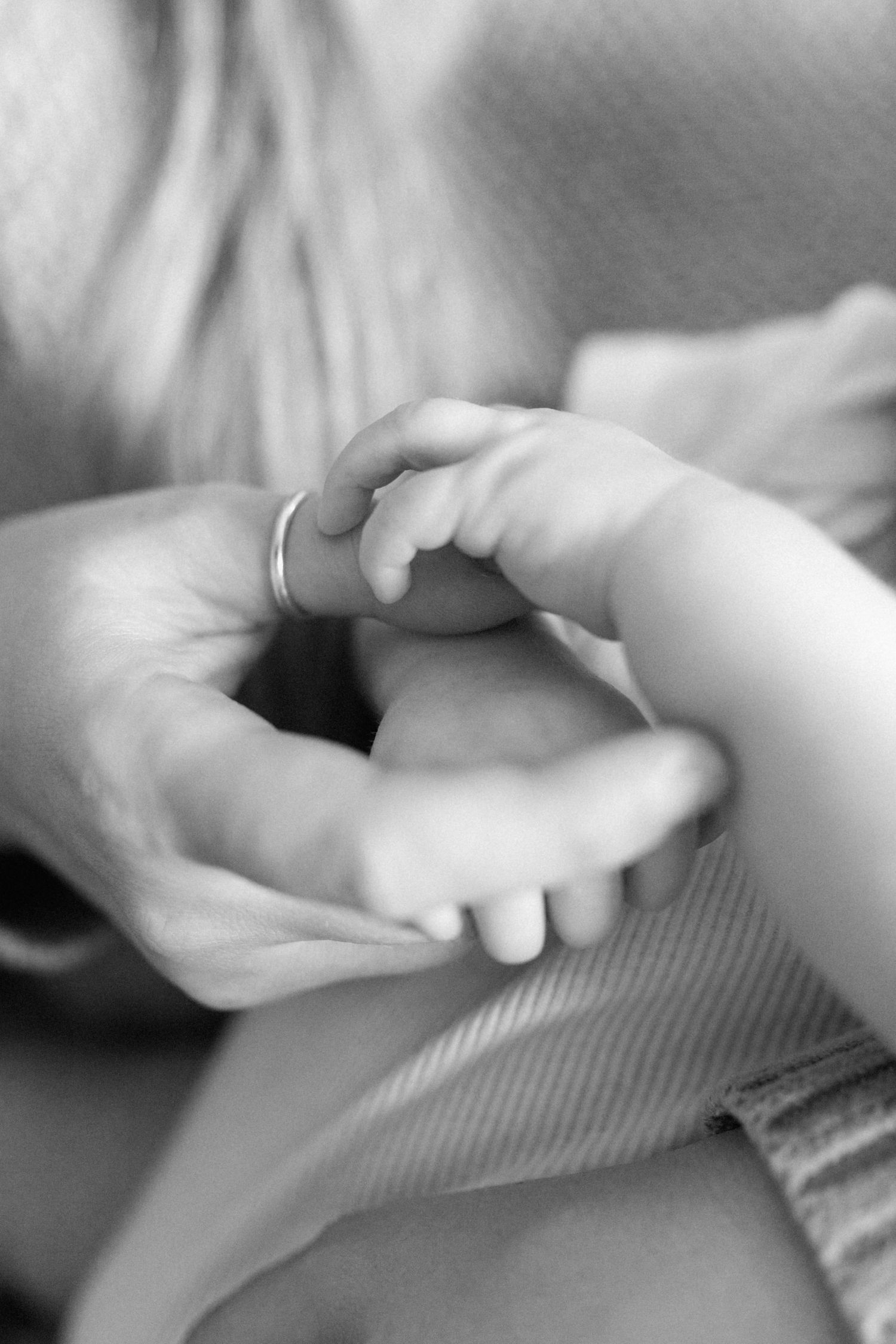 A close up of a newborn's hand reaching out to the ring on their parent's thumb. Photo by Katie Crane Photography.