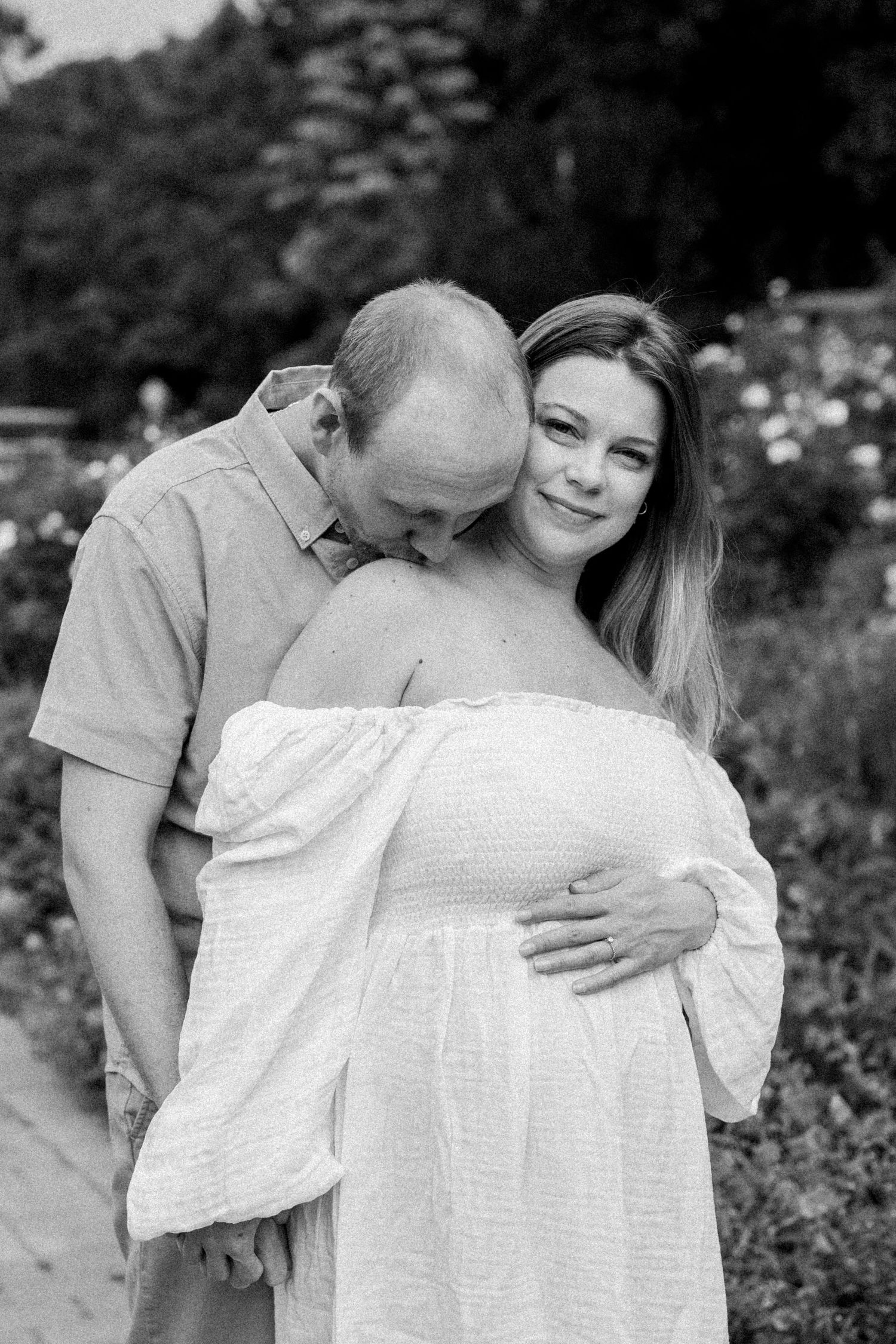 An intimate black and white photo of a couple embracing in a flower garden.