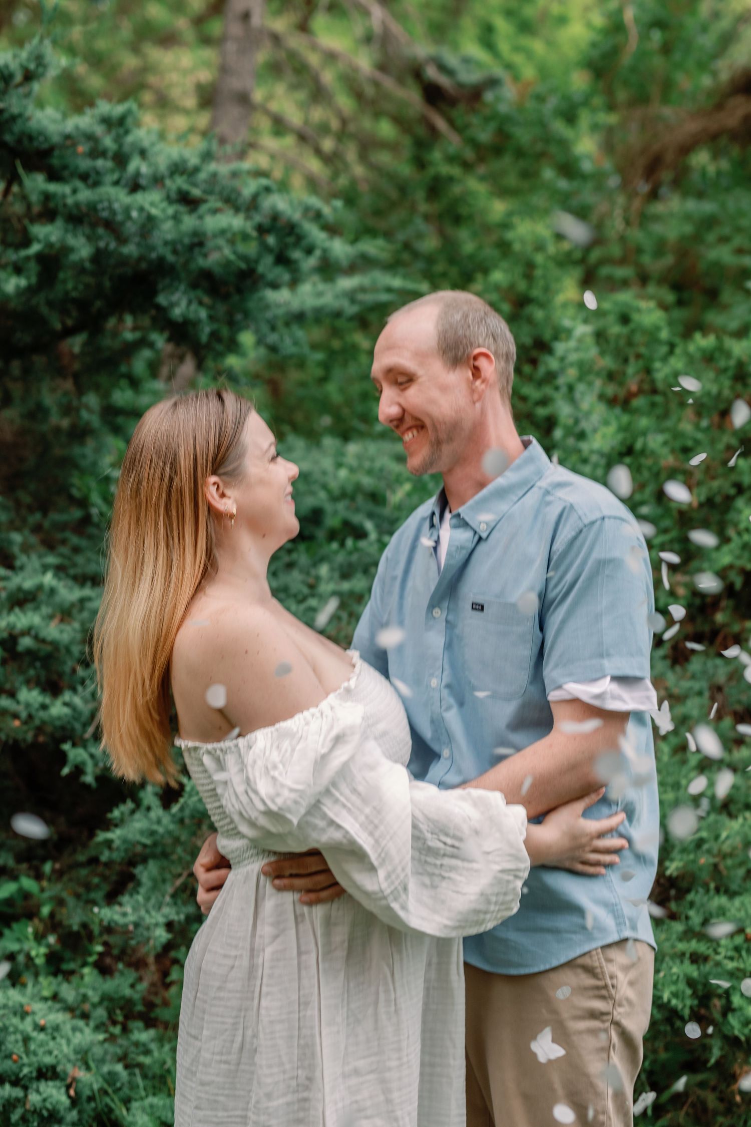 Romantic couple embraces in a lush garden setting wearing white and blue casual attire.