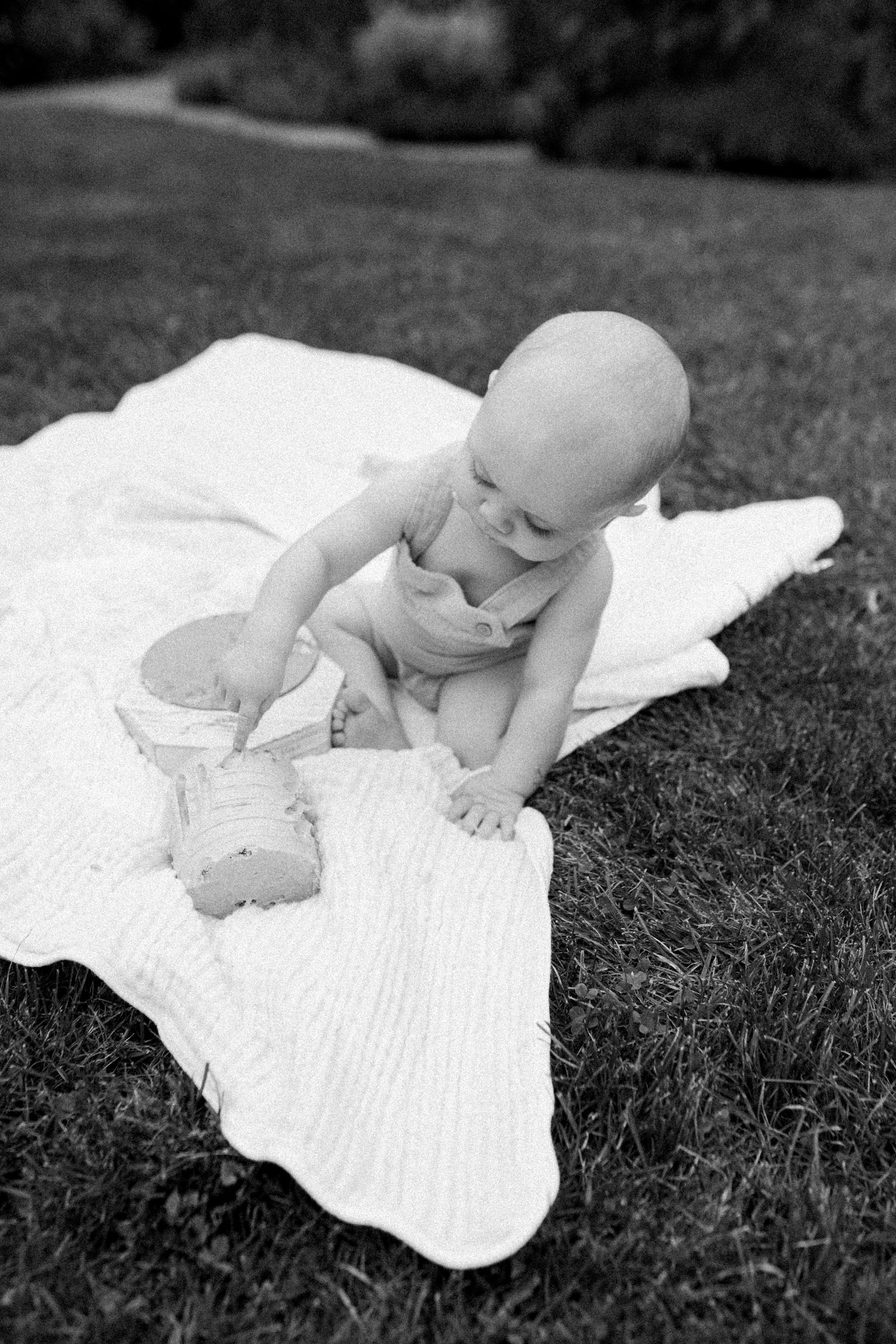 Black and white portrait of baby playing on white blanket outdoors.