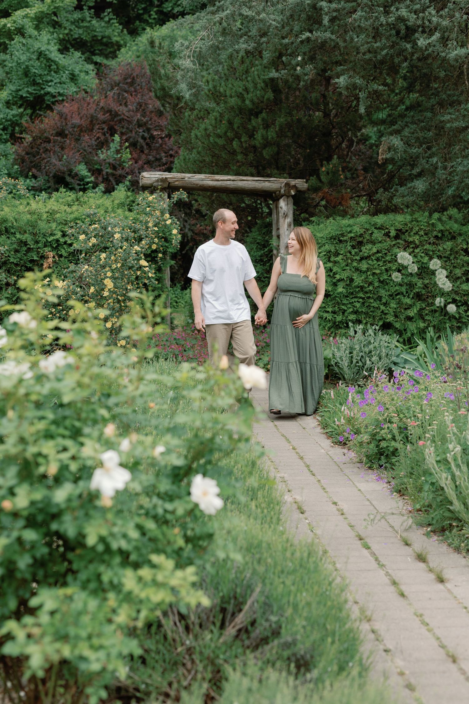Couple strolls along garden path surrounded by blooming flowers.