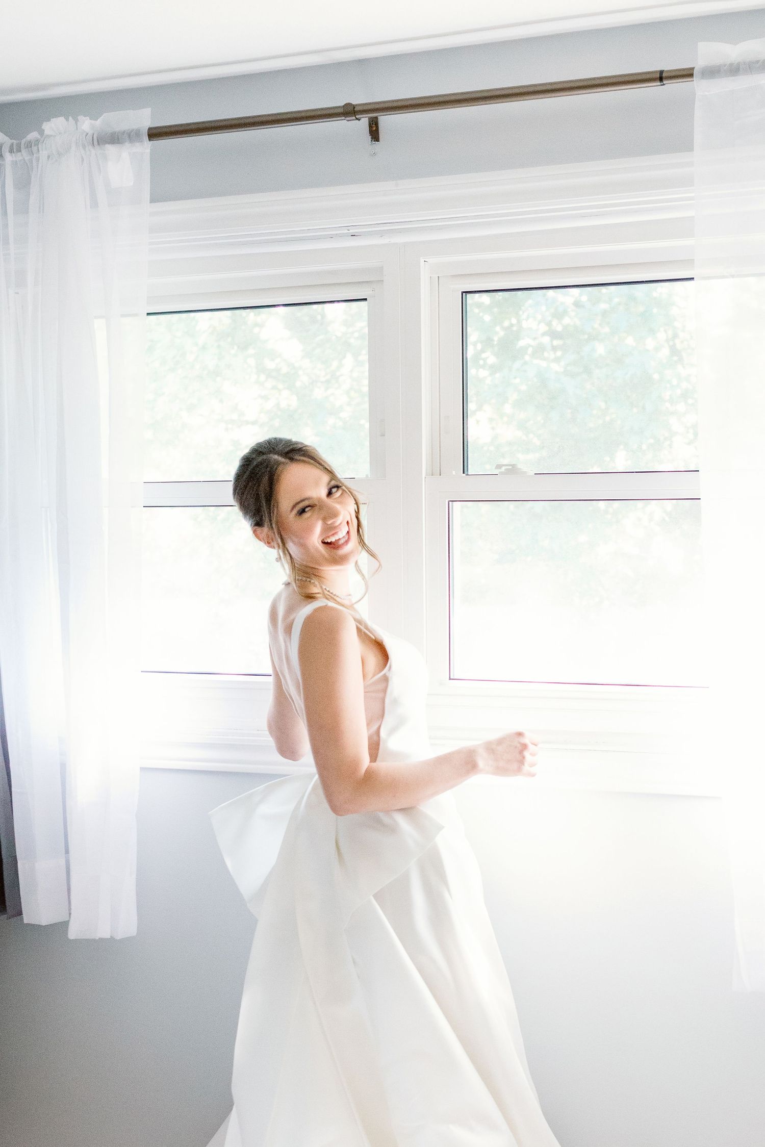 Joyful moment of bride standing by window in beautiful light - Katie Crane Photography, Toronto Candid Wedding and Famil