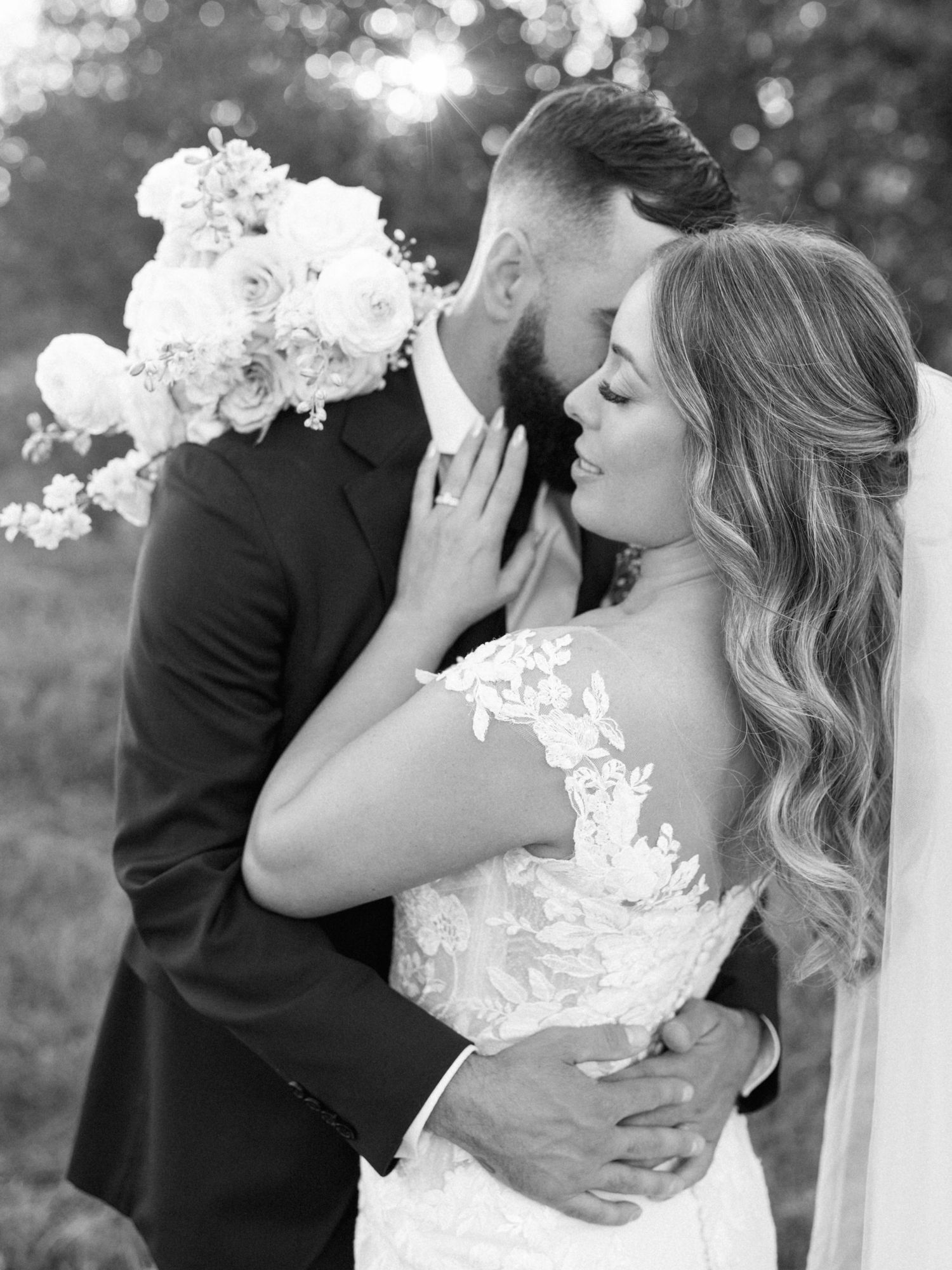 A side view of a bride, eyes closed, held around the waist by her groom face hidden behind hers. Photo taken by Katie Cr