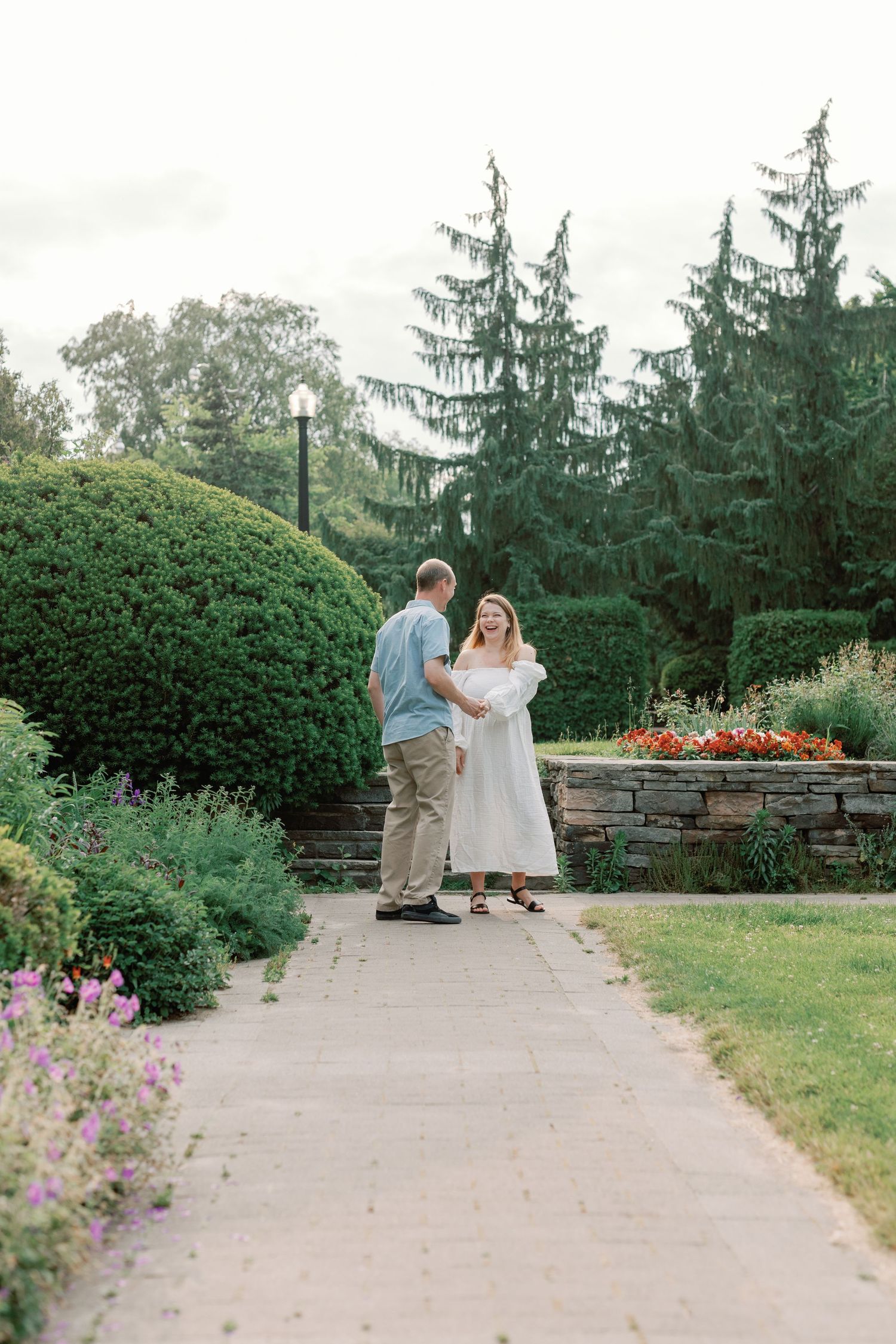 A couple embraces while standing on a stone-lined path in a lush garden setting.