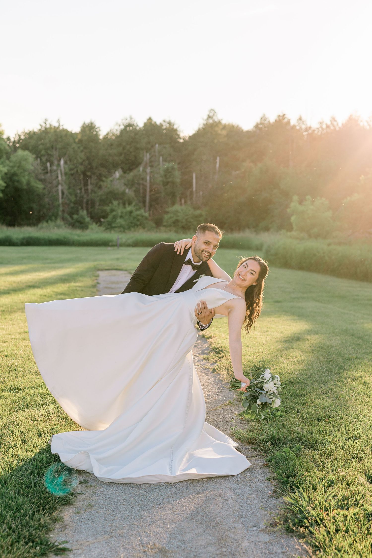 A joyful bride and groom share a romantic dip pose on a garden path during golden hour at their outdoor wedding.