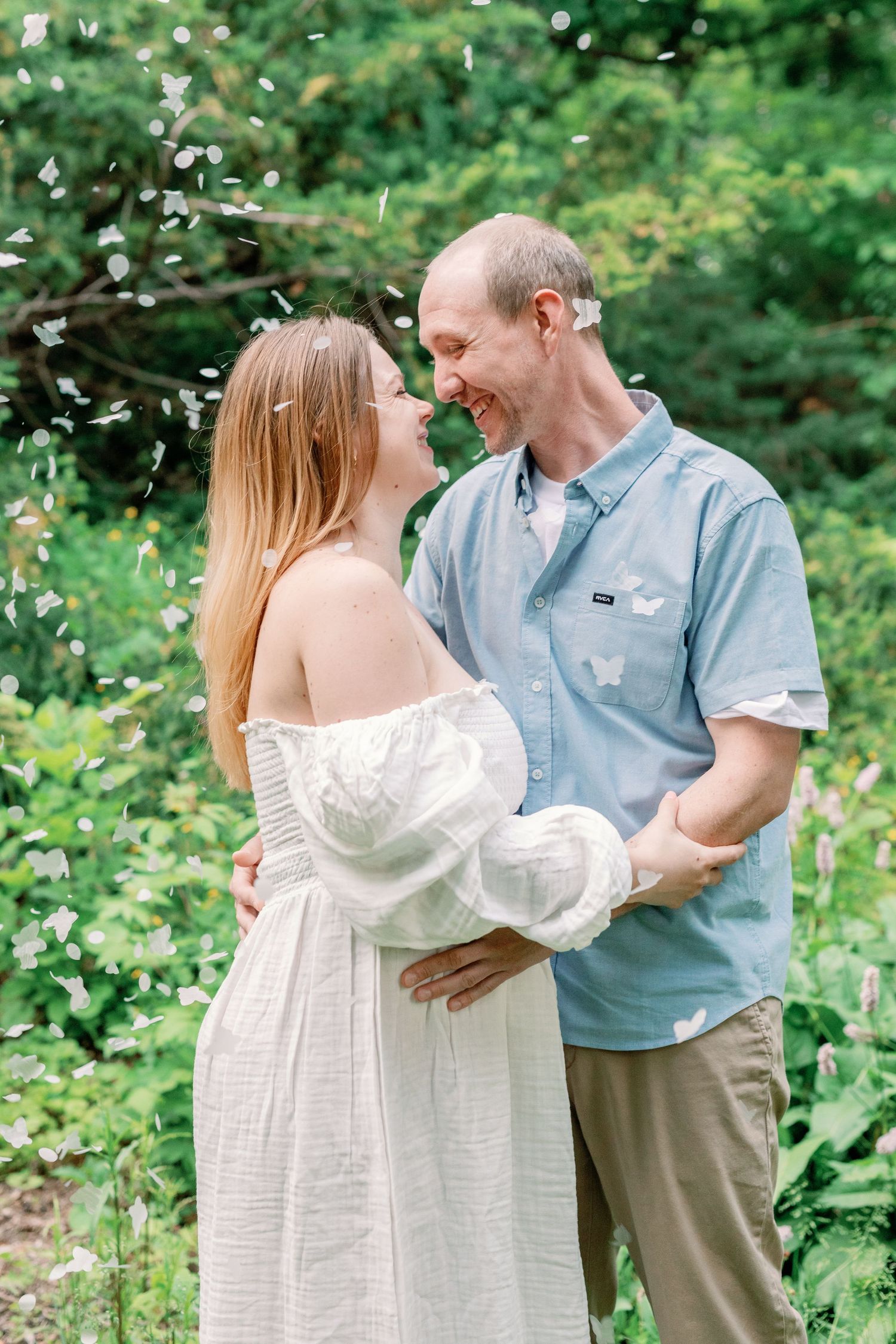 A couple shares a tender moment amid floating confetti in a lush green garden setting.