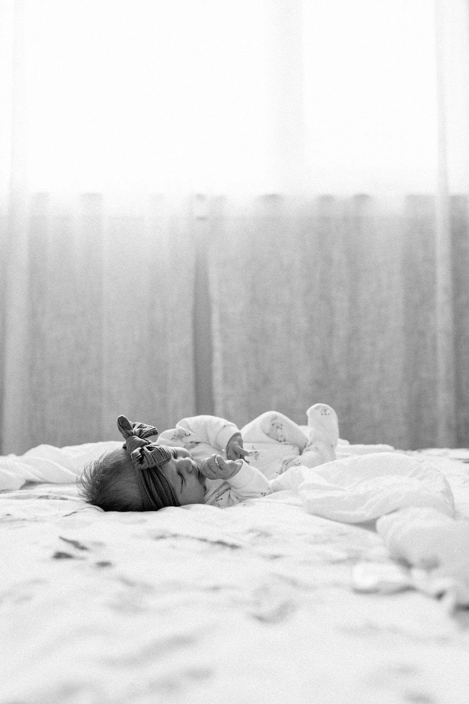 Black and white panorama of infant resting on white bedding.