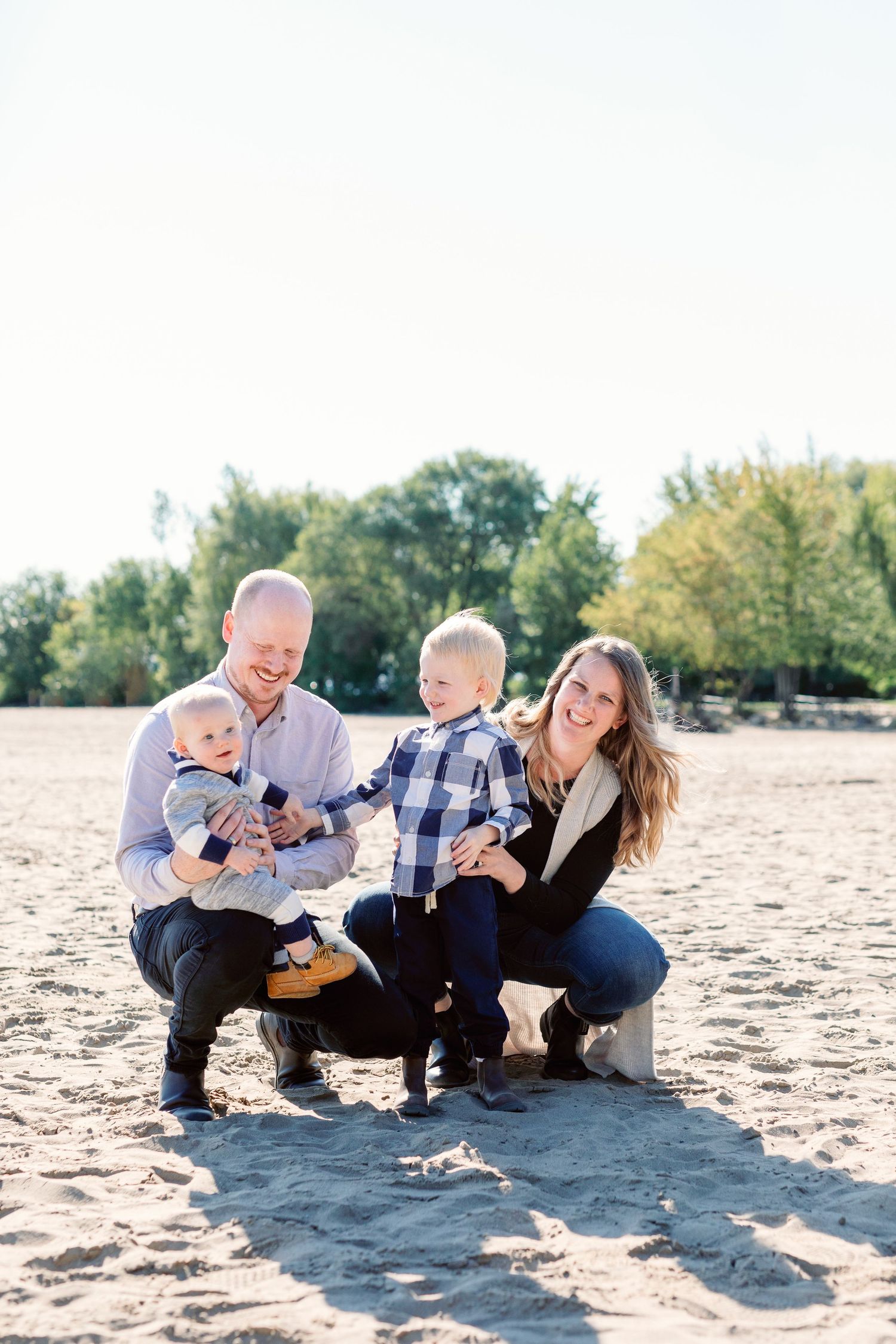 Family playing and laughing together on sandy beach in bright sunlight.