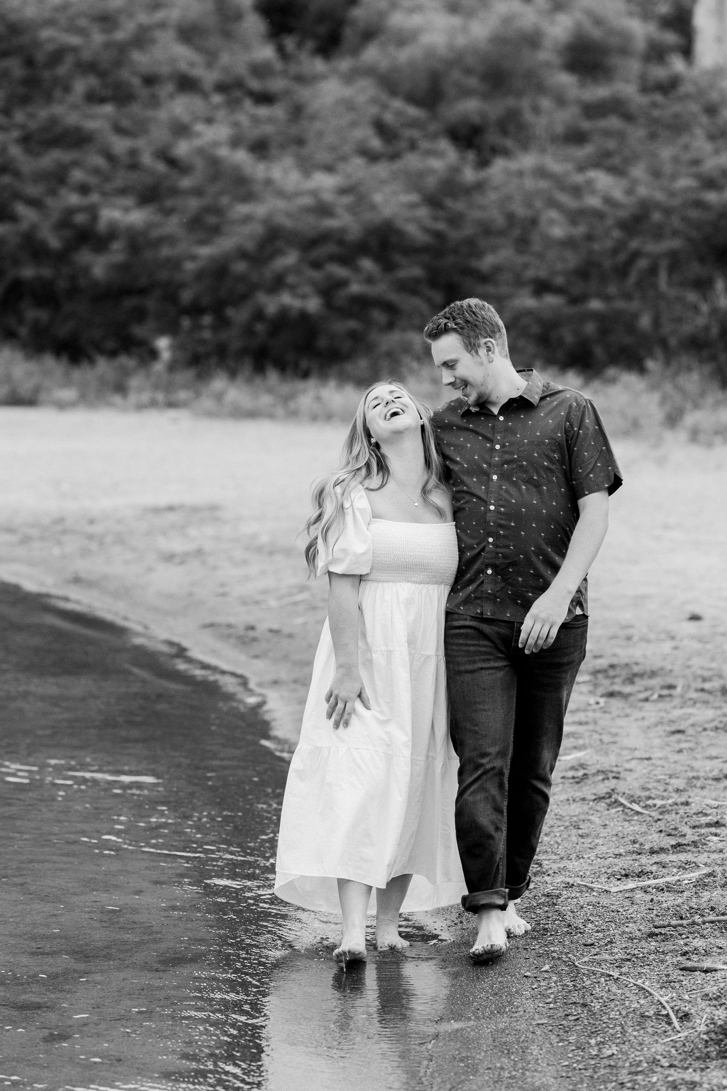 A couple shares a tender moment at the water's edge in black and white photography.