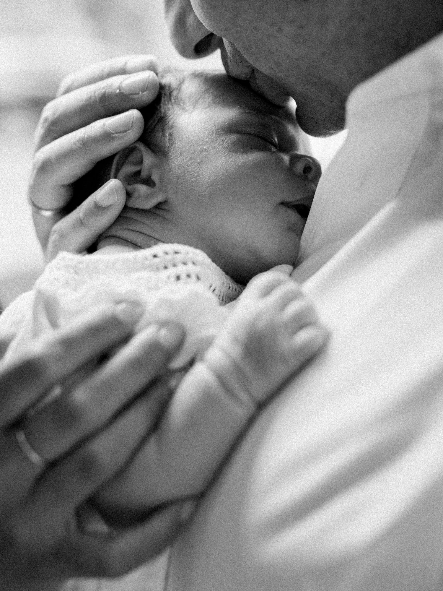 Black and white intimate portrait of a newborn being tenderly held.