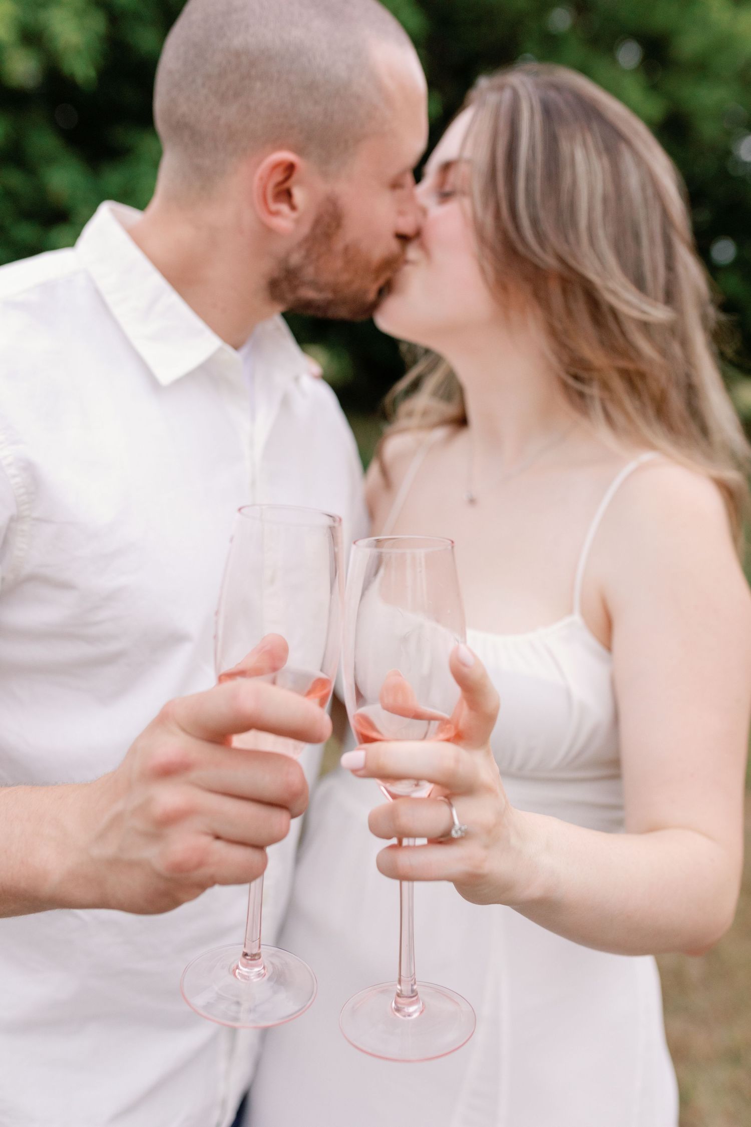 Couple toasting with pink champagne glasses while sharing intimate moments outdoors.