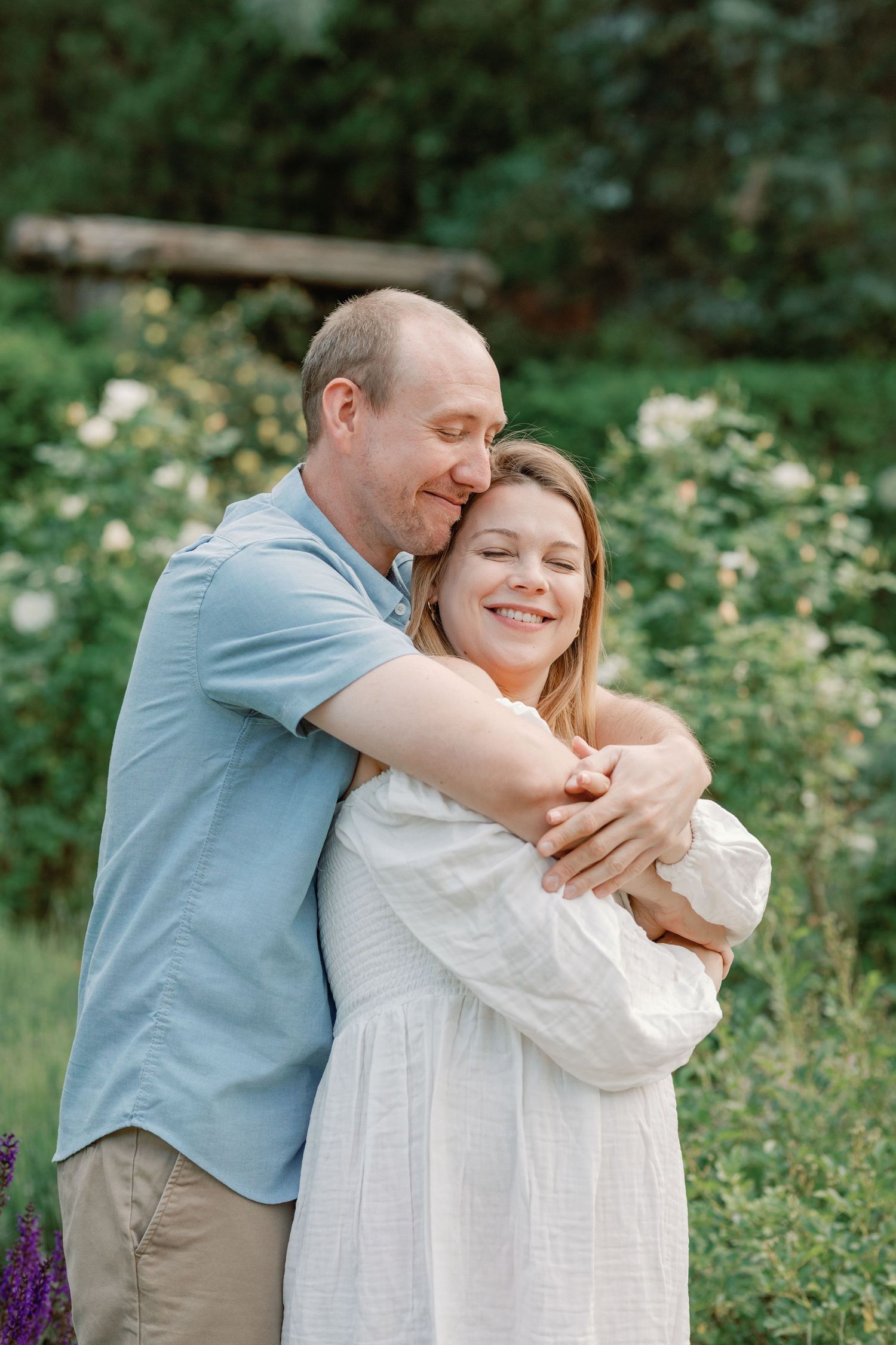 A couple shares a joyful embrace among blooming flowers in a summer garden.
