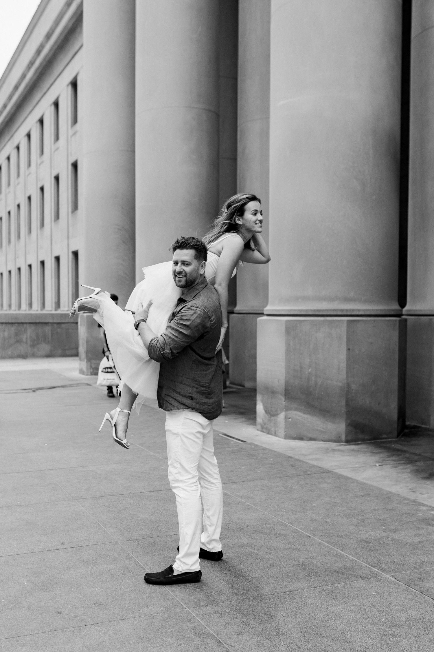 A black and white photo of a playful pose against classical architecture with tall columns.