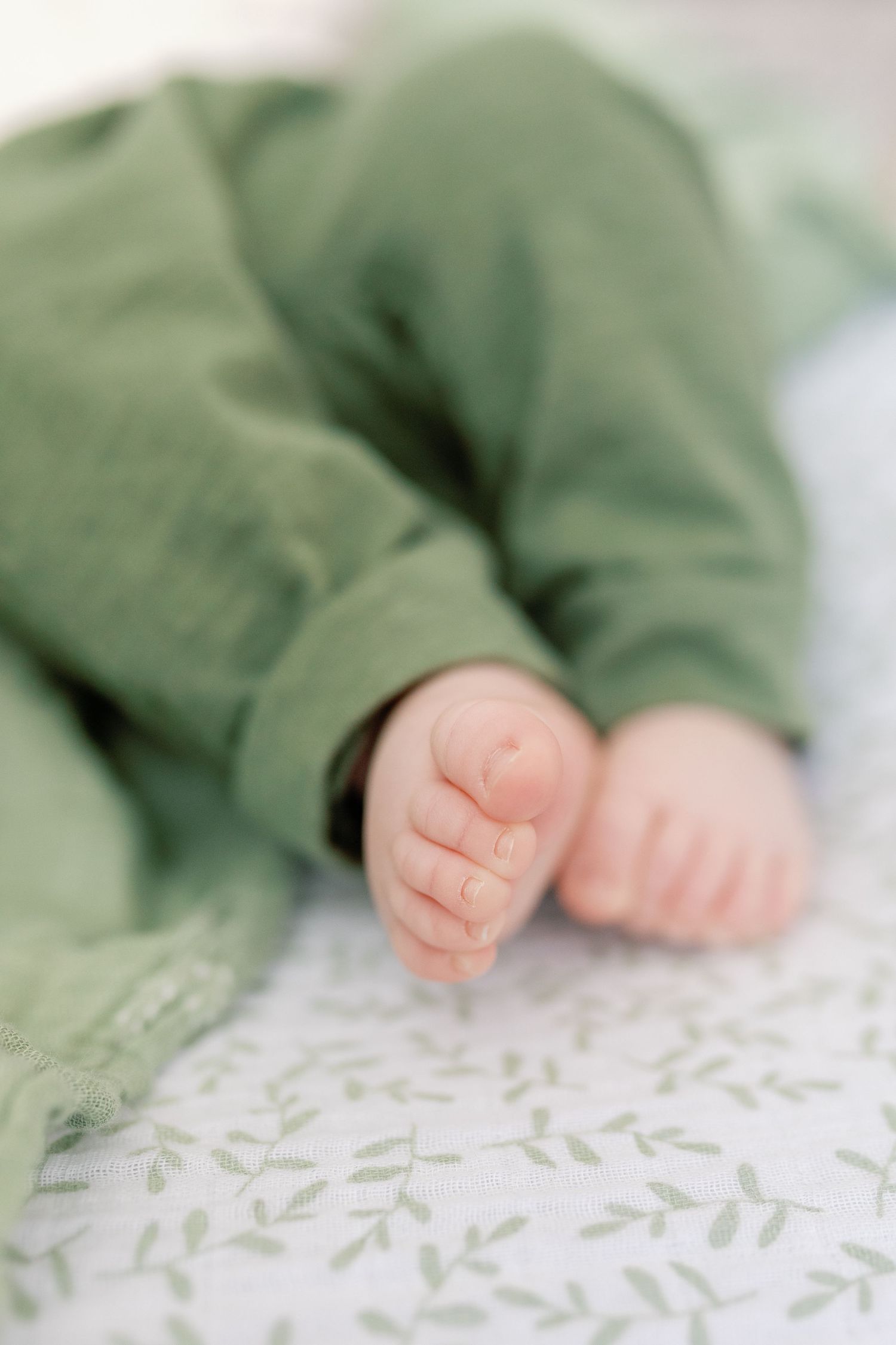A close photo of a newborn's legs in green pants, stretched out on the bed. Photo by Katie Crane Photography.