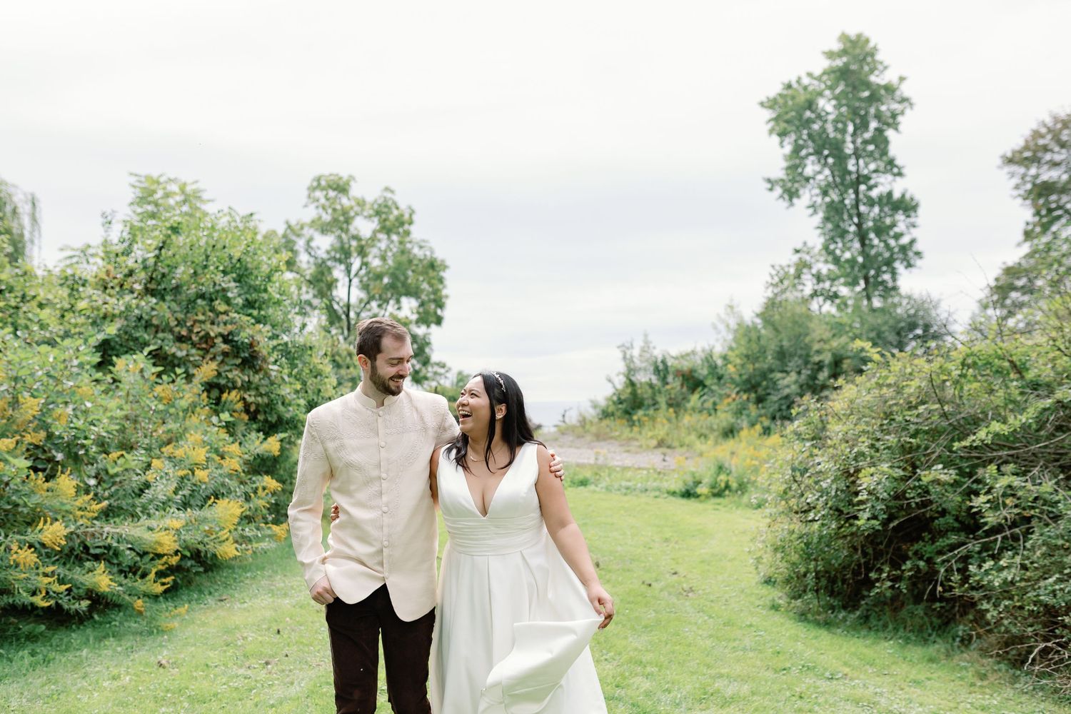 A couple in their wedding outfits walk through a park, arms around each other. Photo by Katie Crane Photography.