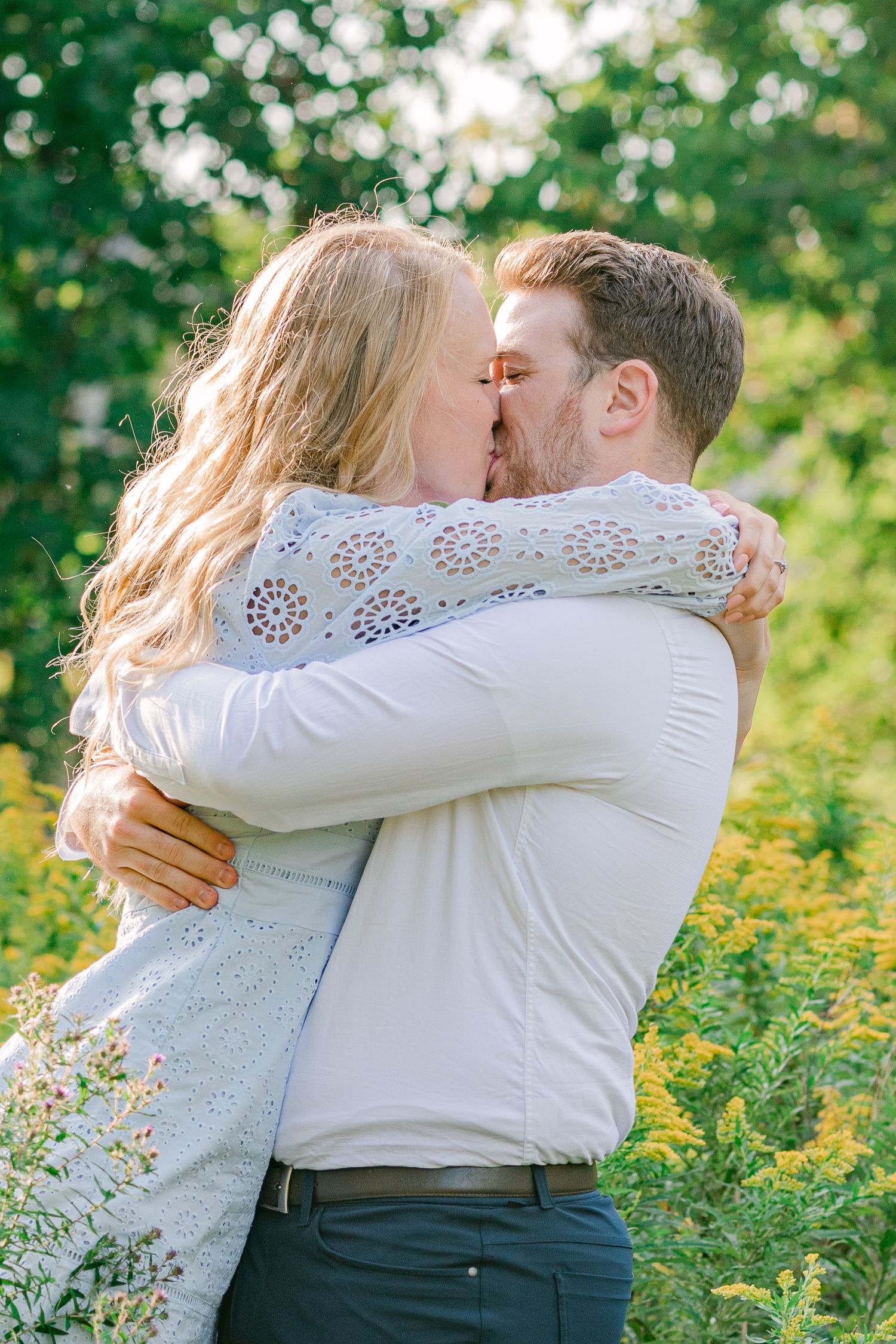 Couple embracing in a field of wildflowers wearing white summer attire.