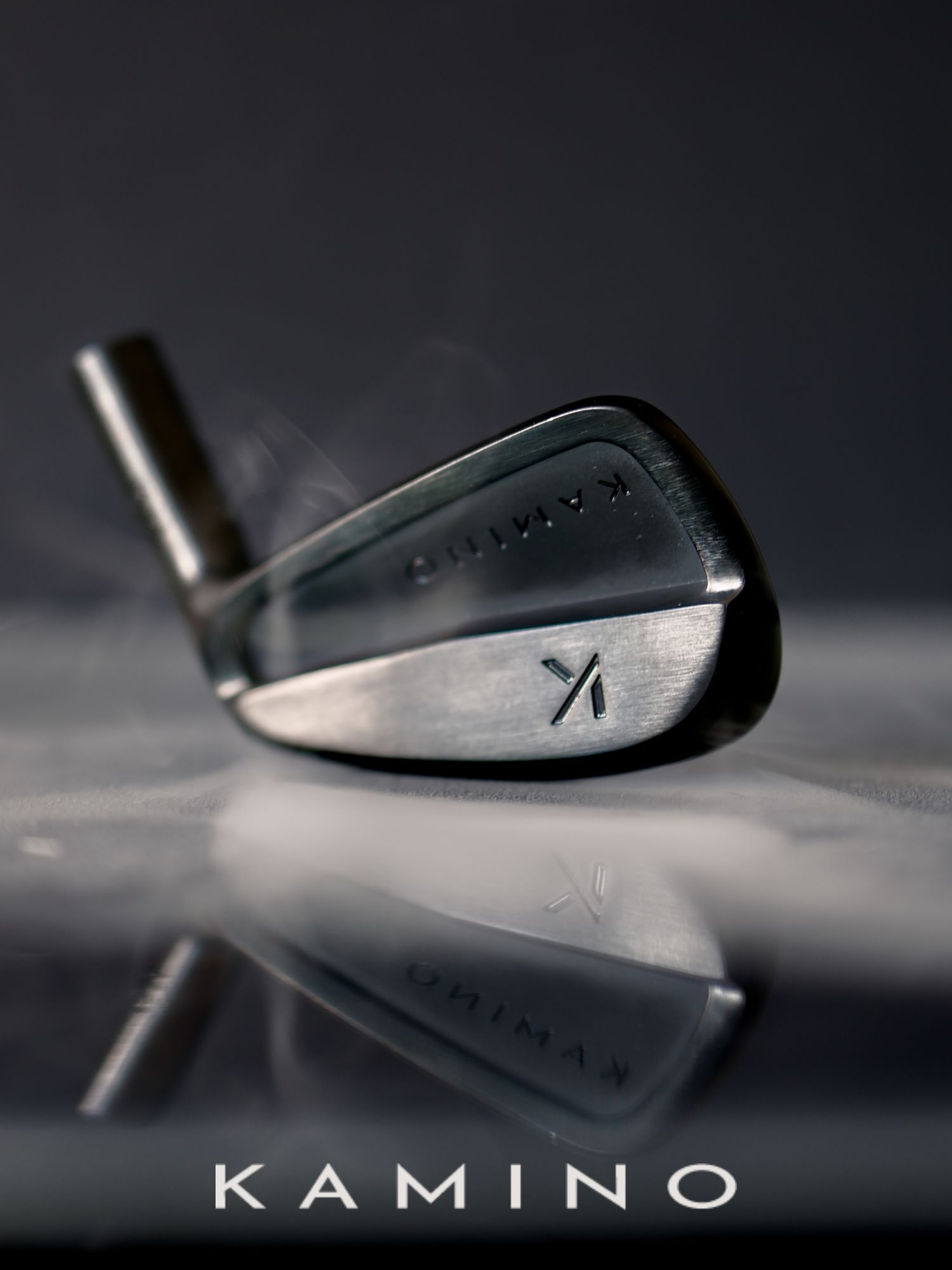Kamino golf iron club head with brushed steel finish displayed on reflective surface against dark background.
