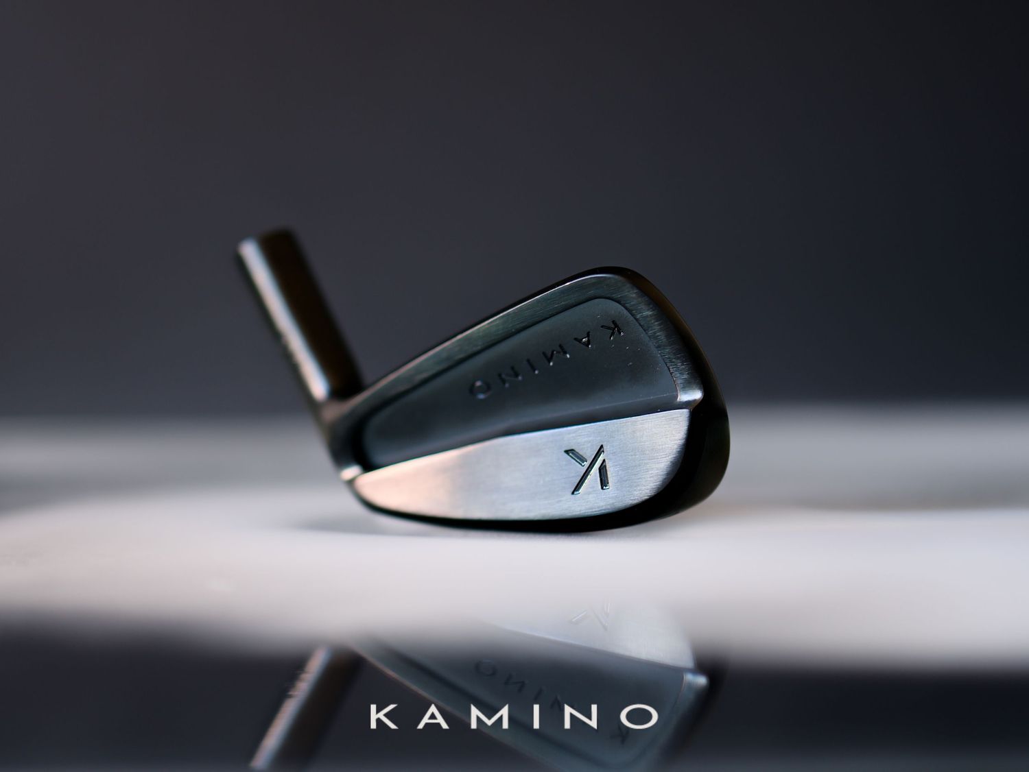 Sleek Kamino Golf iron club reflecting on a glossy surface against a dark background.