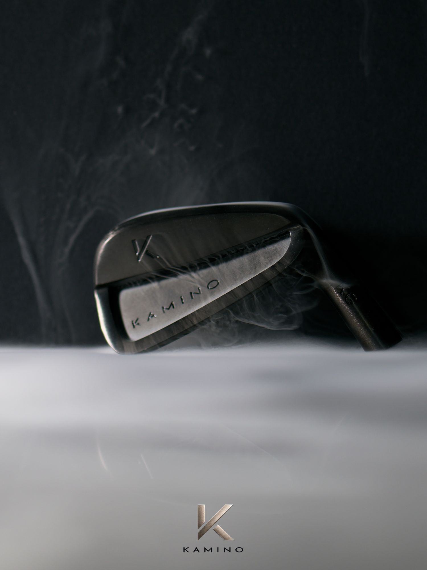 Kamino Golf iron club head emerging from white smoke against a dark dramatic background.
