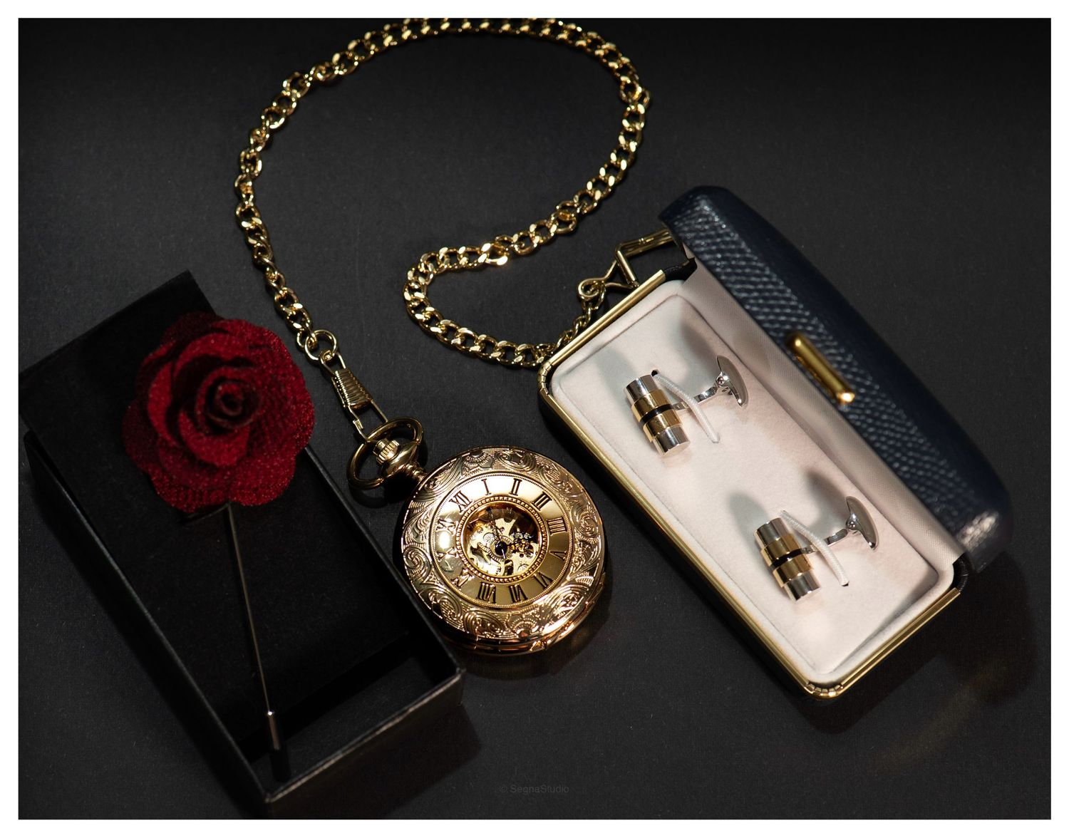 Gold pocket watch with chain next to a red rose and a gift box on black background.