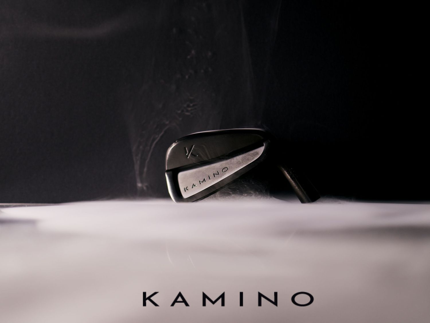 Kamino Golf iron club head surrounded by white smoke on a dark dramatic background.