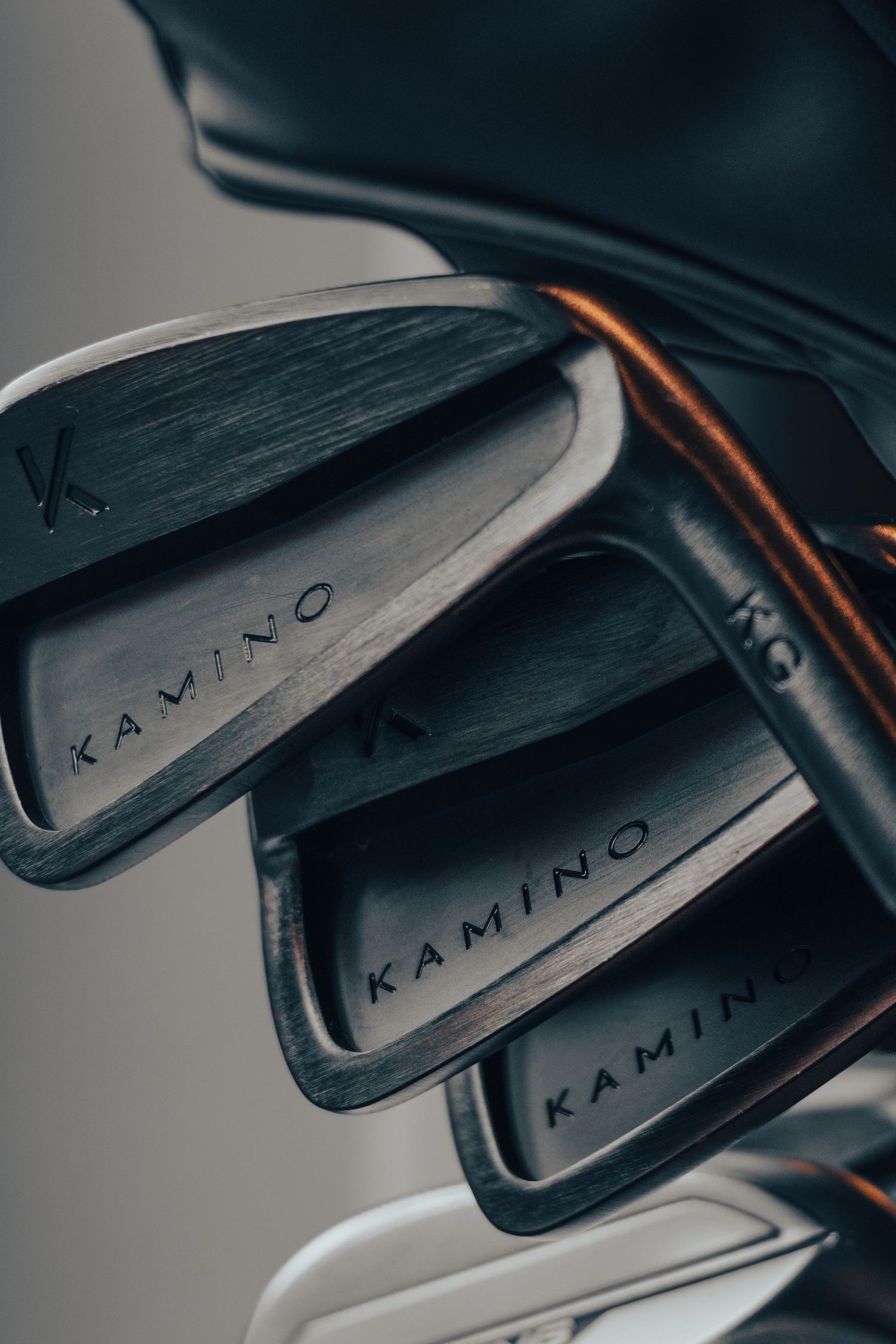 Close-up of Kamino branded dark metal golf irons stacked in a golf bag with brown leather trim.