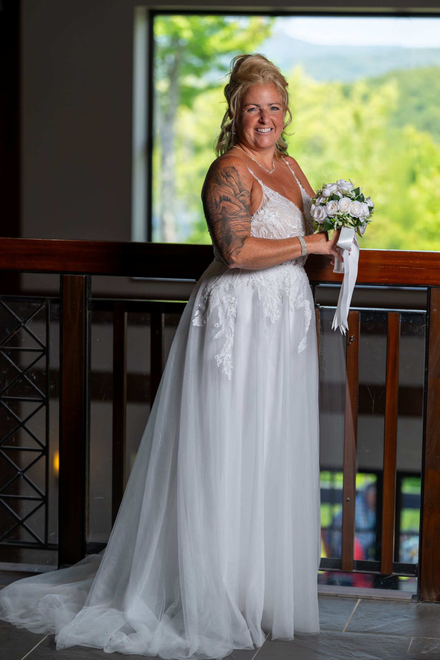 Bridal portrait of a bride holding her bouquet standing near a window with forest views