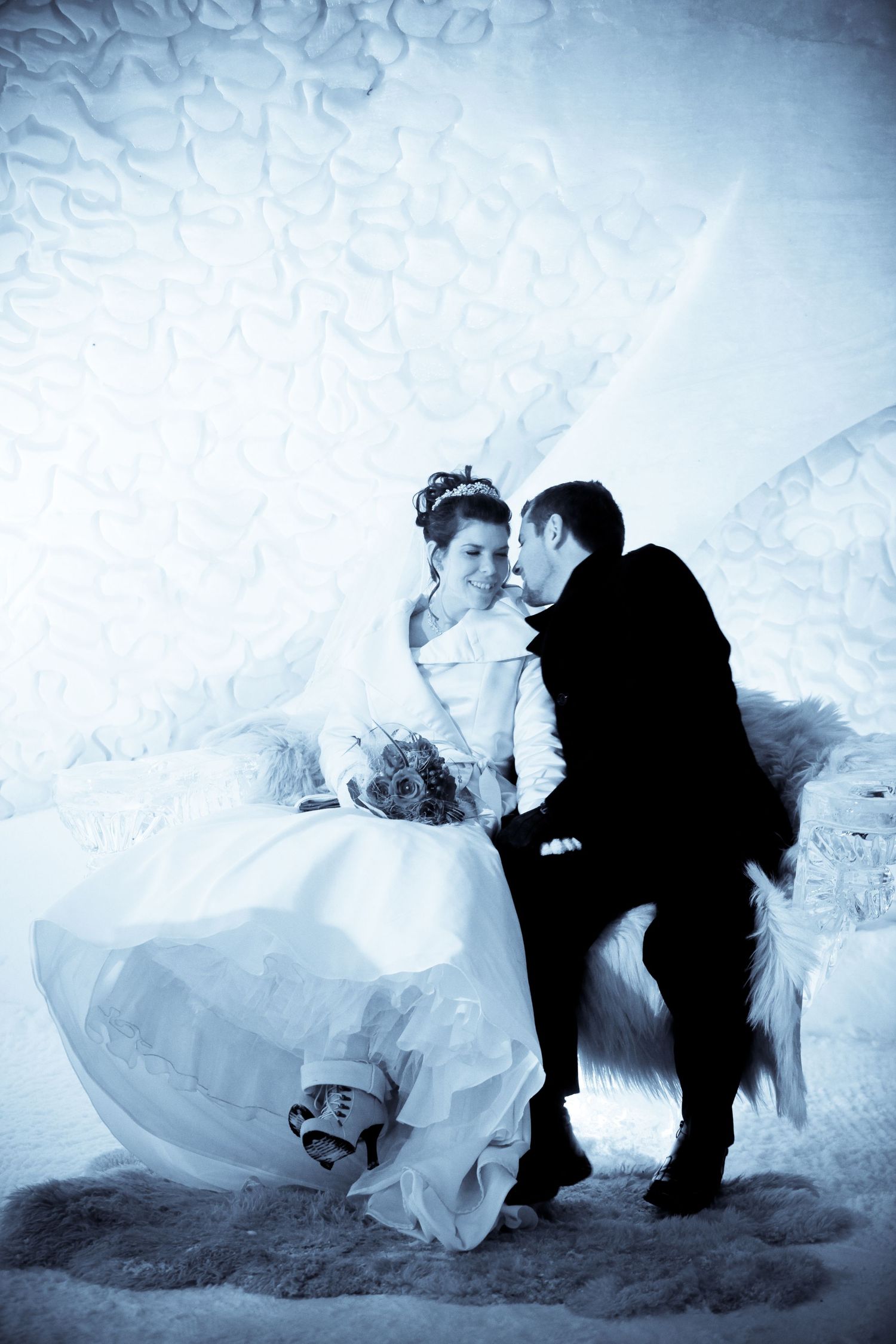 Intimate winter wedding portrait seated inside a blue-lit ice chamber at Hôtel de Glace