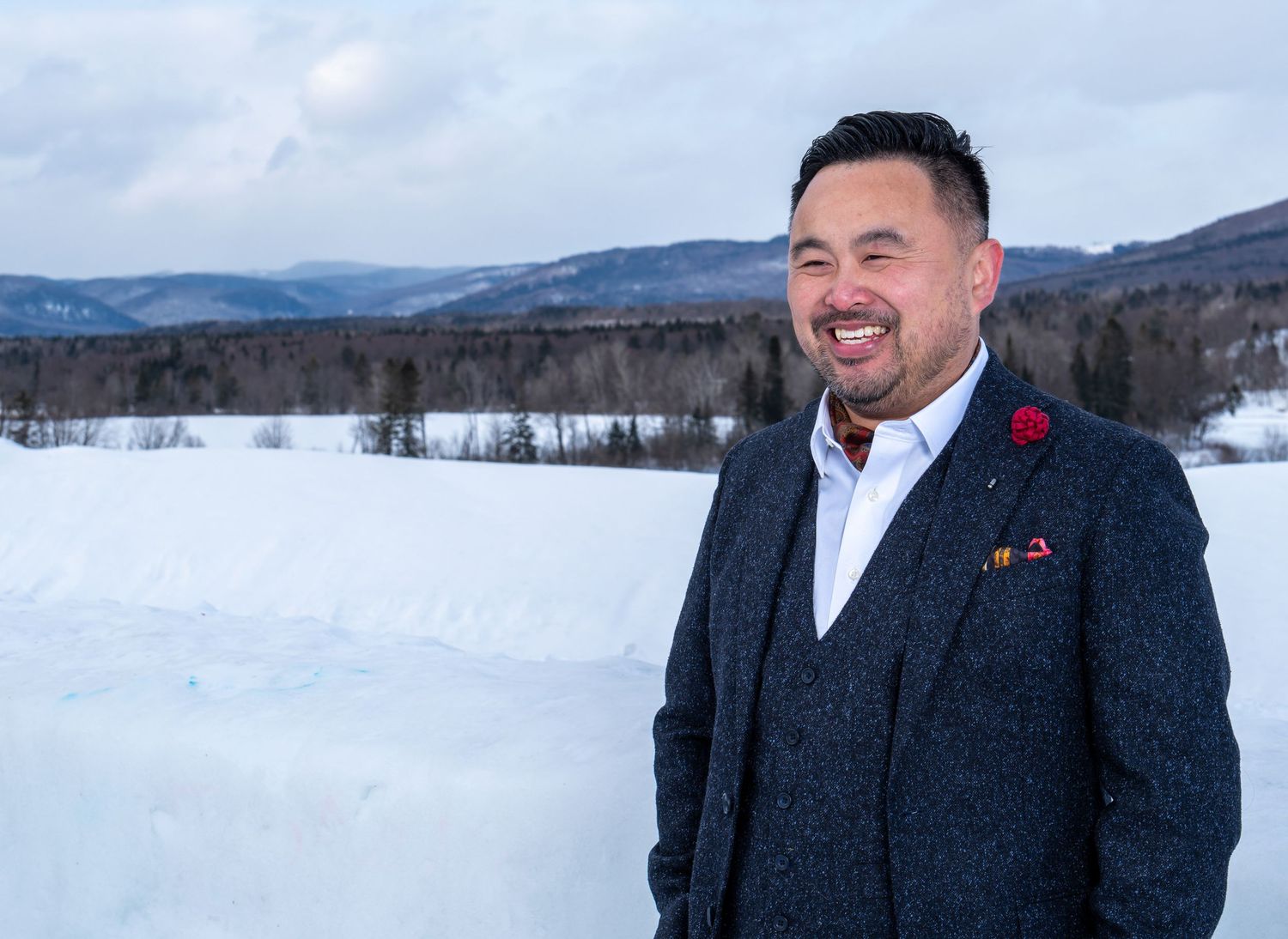 Smiling groom in a dark suit posed against a snowy mountain backdrop for a winter destination wedding