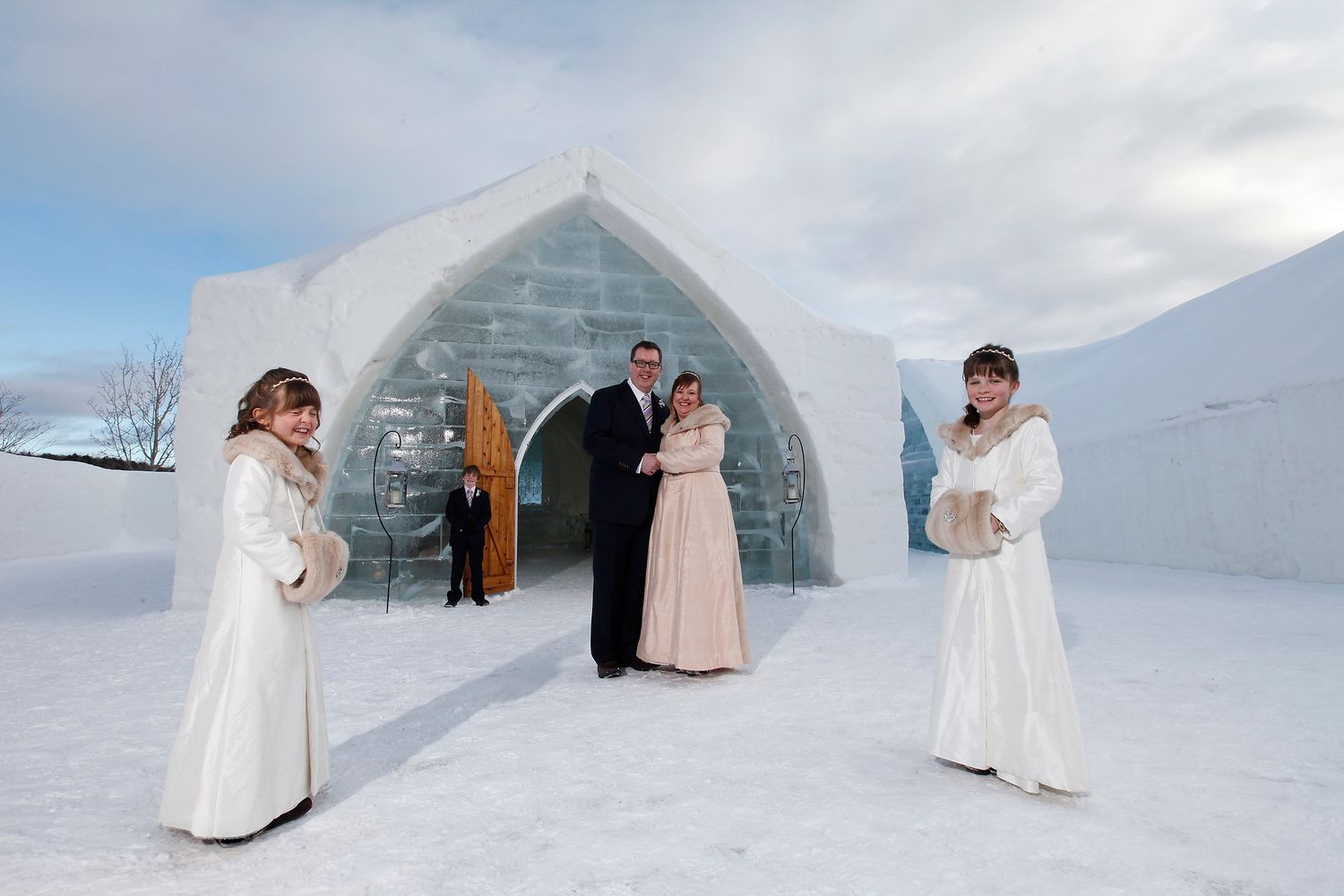 A wedding party posing outside the monumental ice entrance of the Hôtel de Glace in Quebec