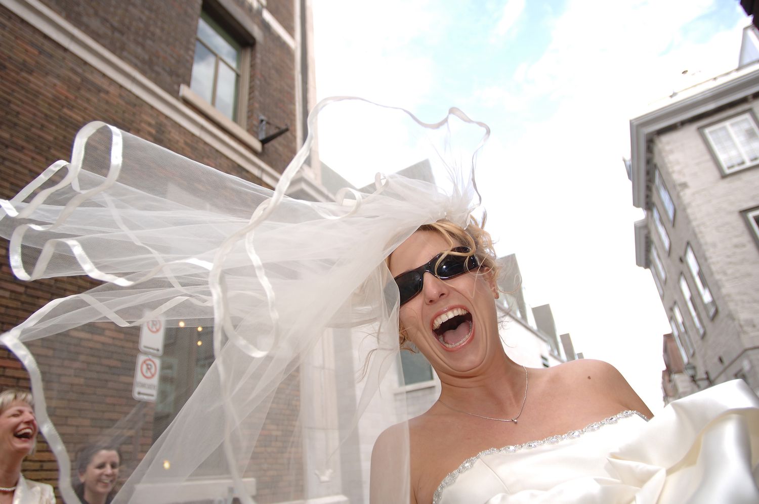 Playful bride laughing with sunglasses and a floating veil in the streets of Old Quebec