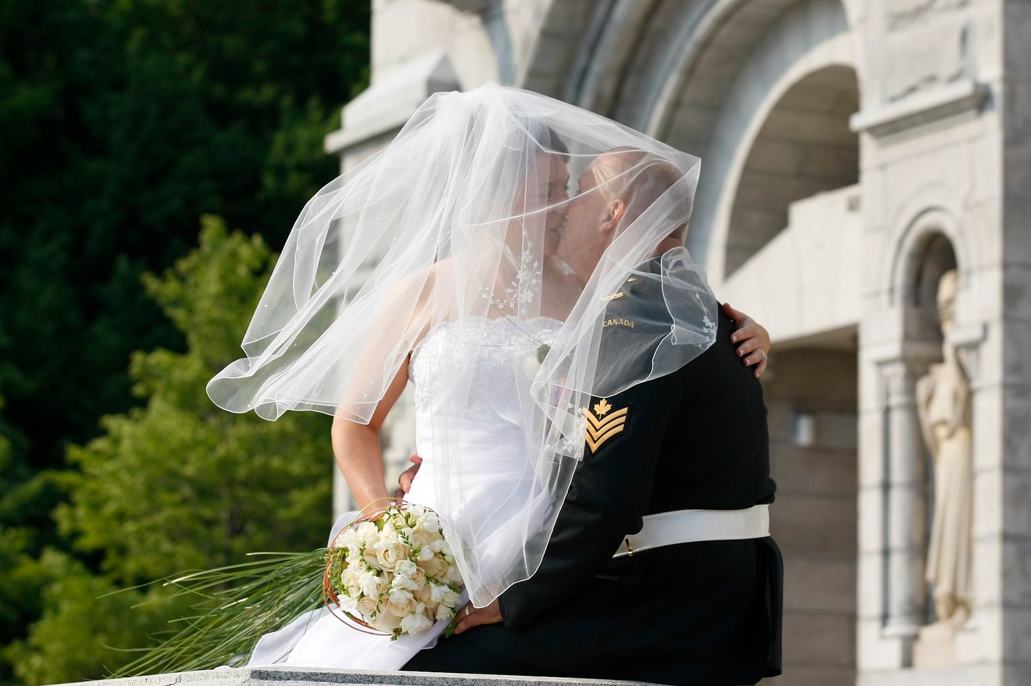 Romantic portrait of a bride under her veil embracing her groom by historic stone arches