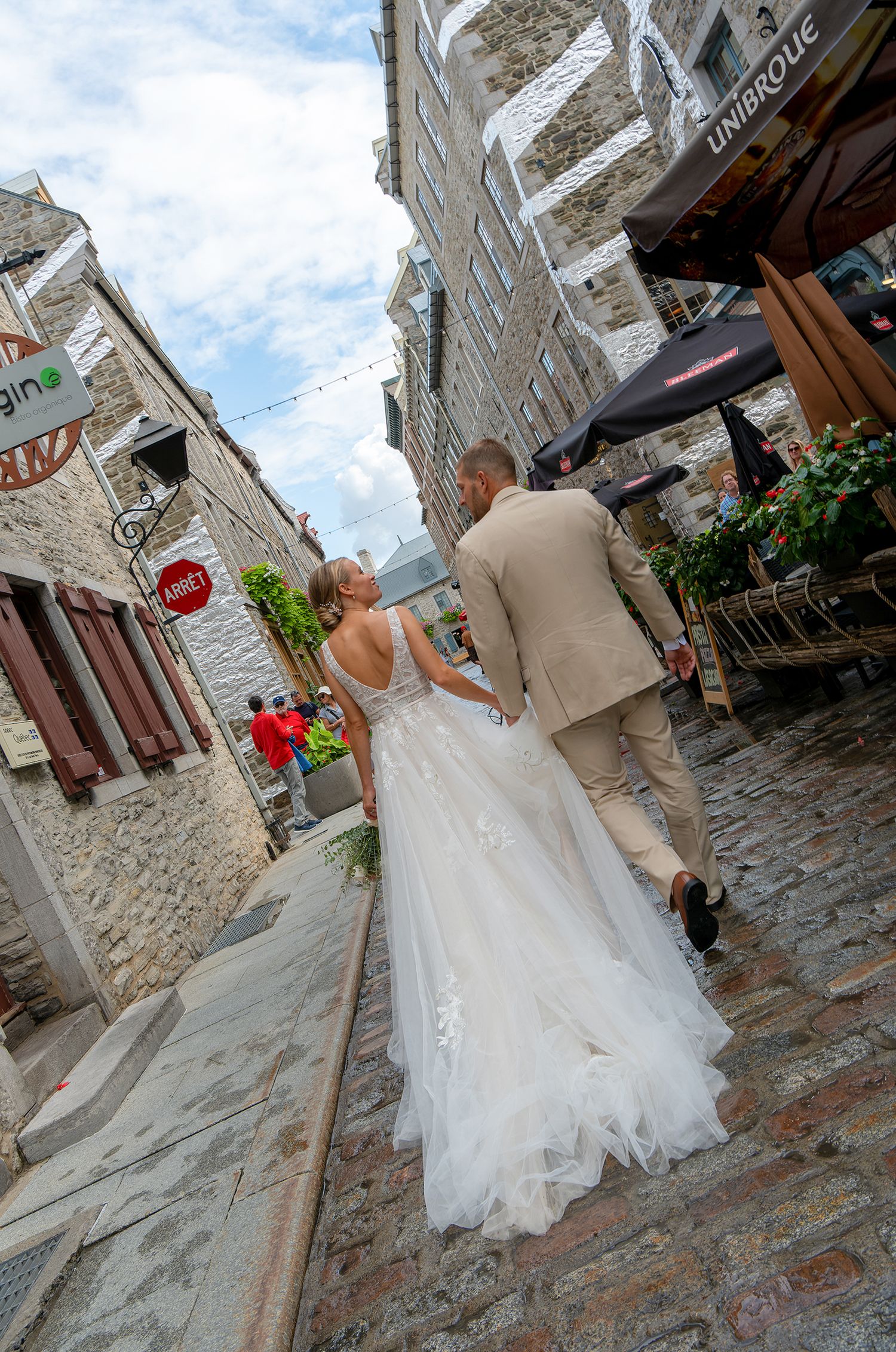 Romantic rear view of a bride and groom walking down a historic cobblestone street in Old Quebec