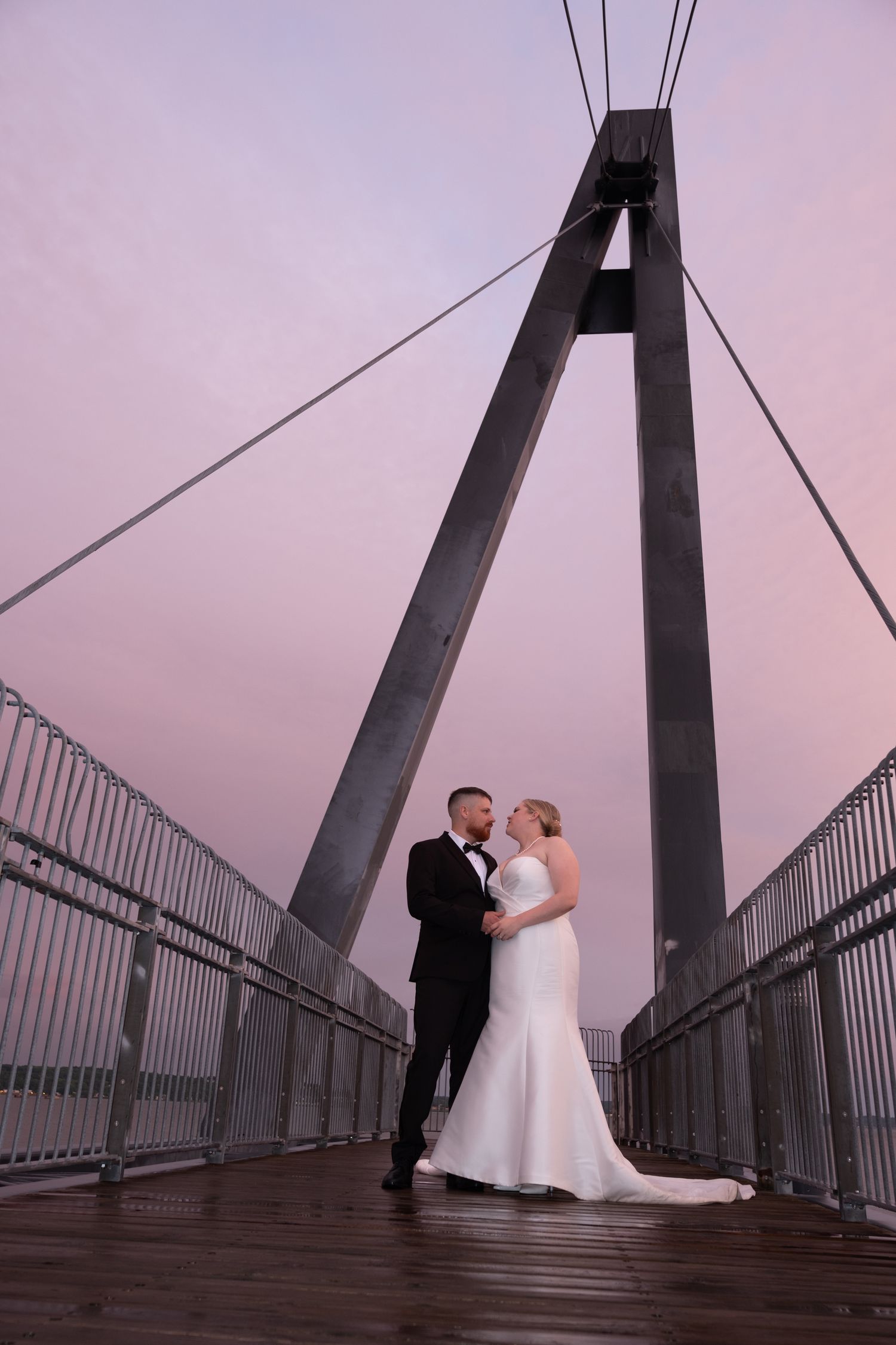Modern wedding photo of a couple standing on a large suspension bridge at dusk