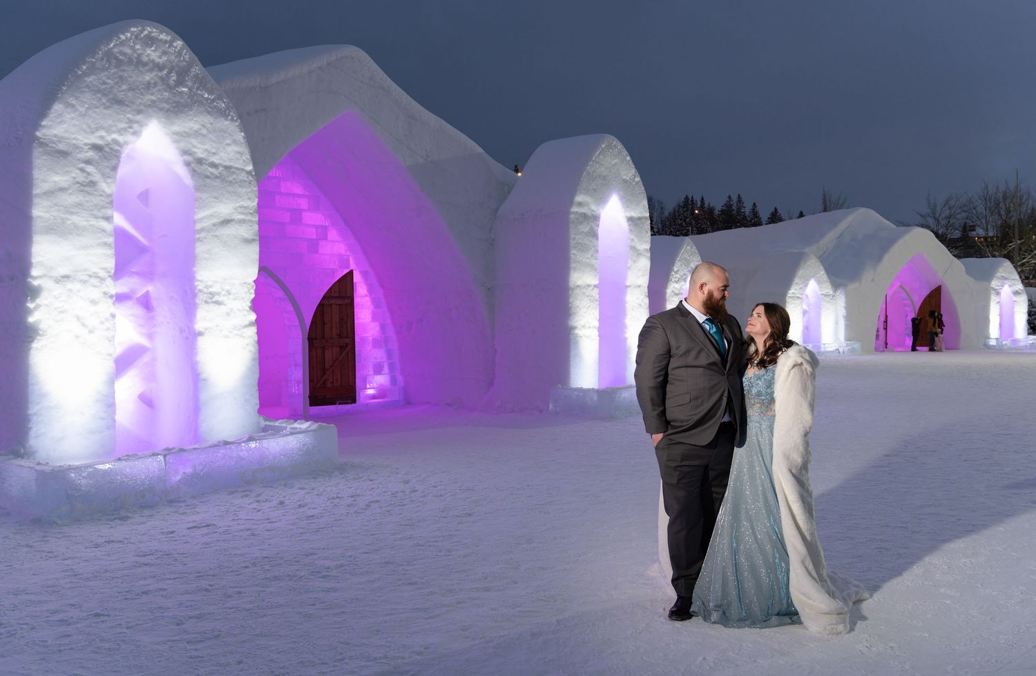 Couple outside the main illuminated ice entrance of the Hôtel de Glace, Quebec City, at dusk